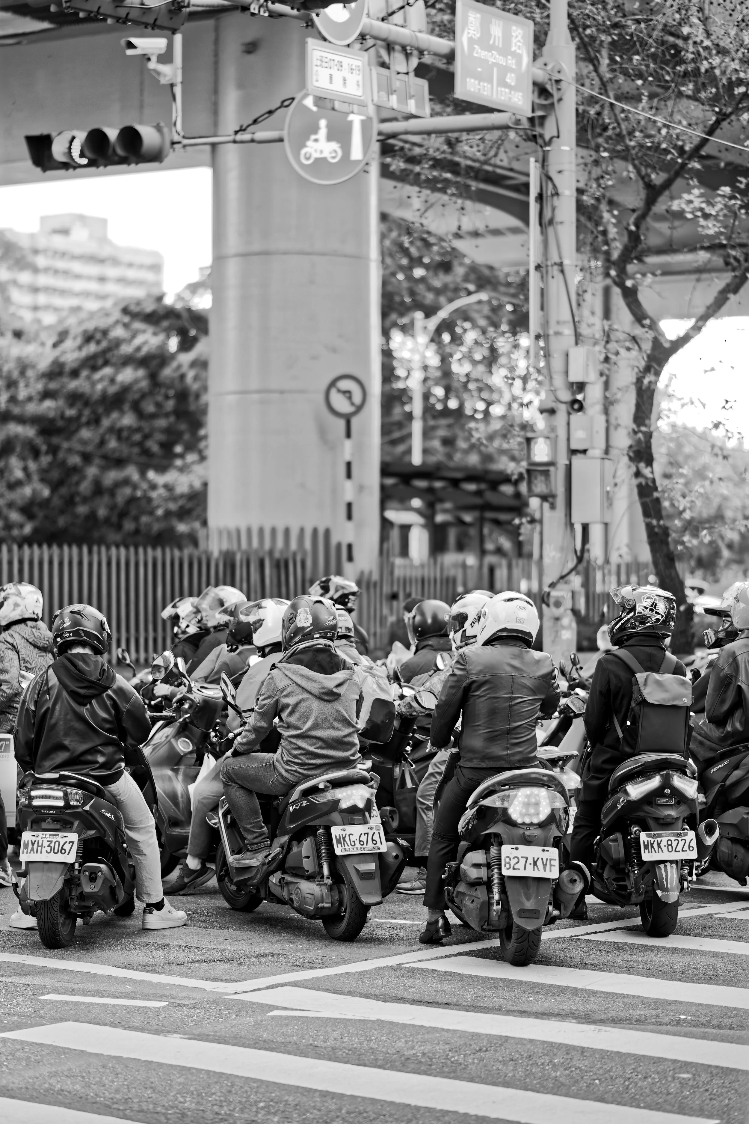 A group of motorcyclists wearing helmets and jackets waiting at a traffic light at an intersection.