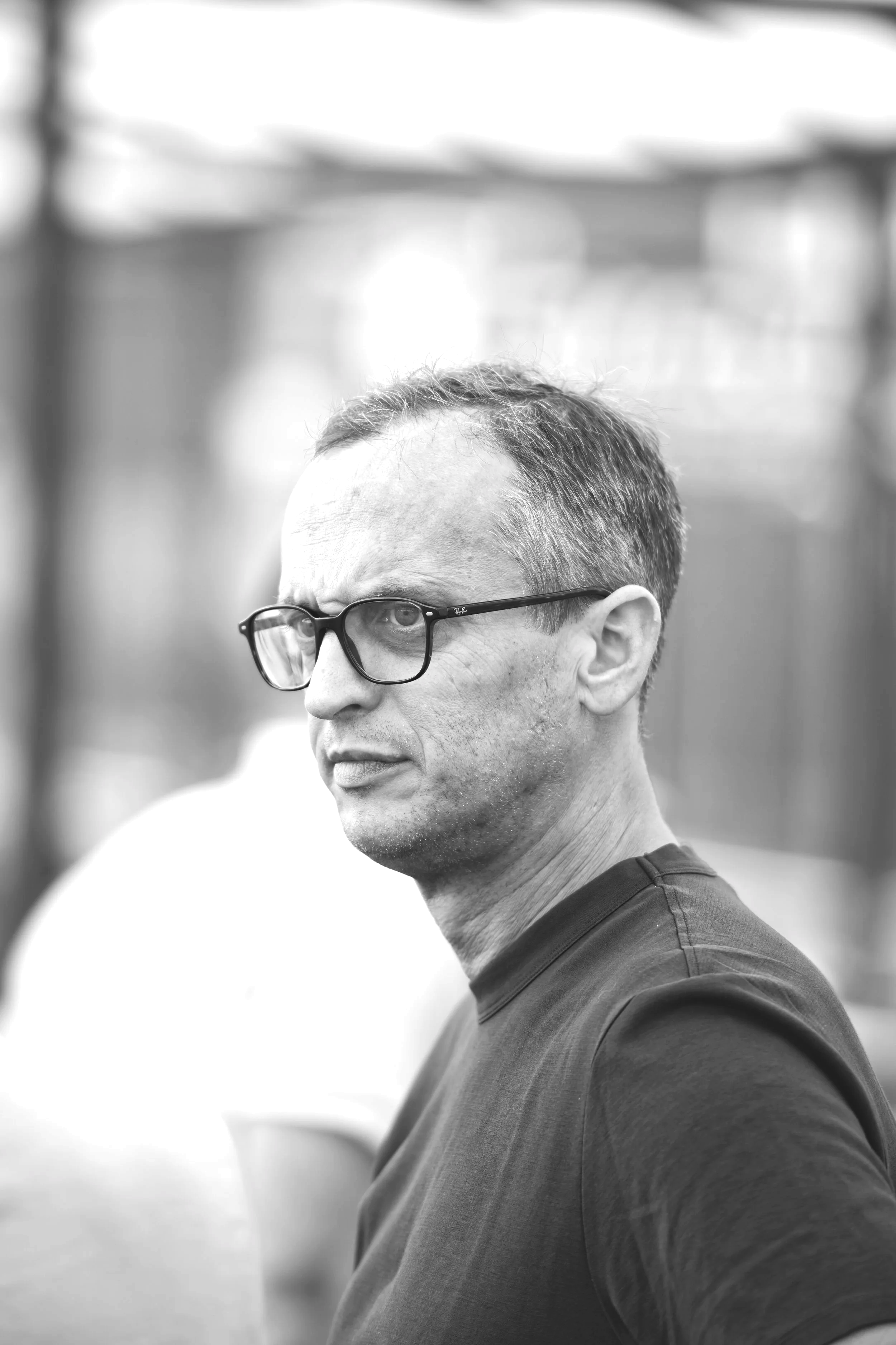 Black and white photo of a man with glasses, short hair, and a serious expression, looking to the side.