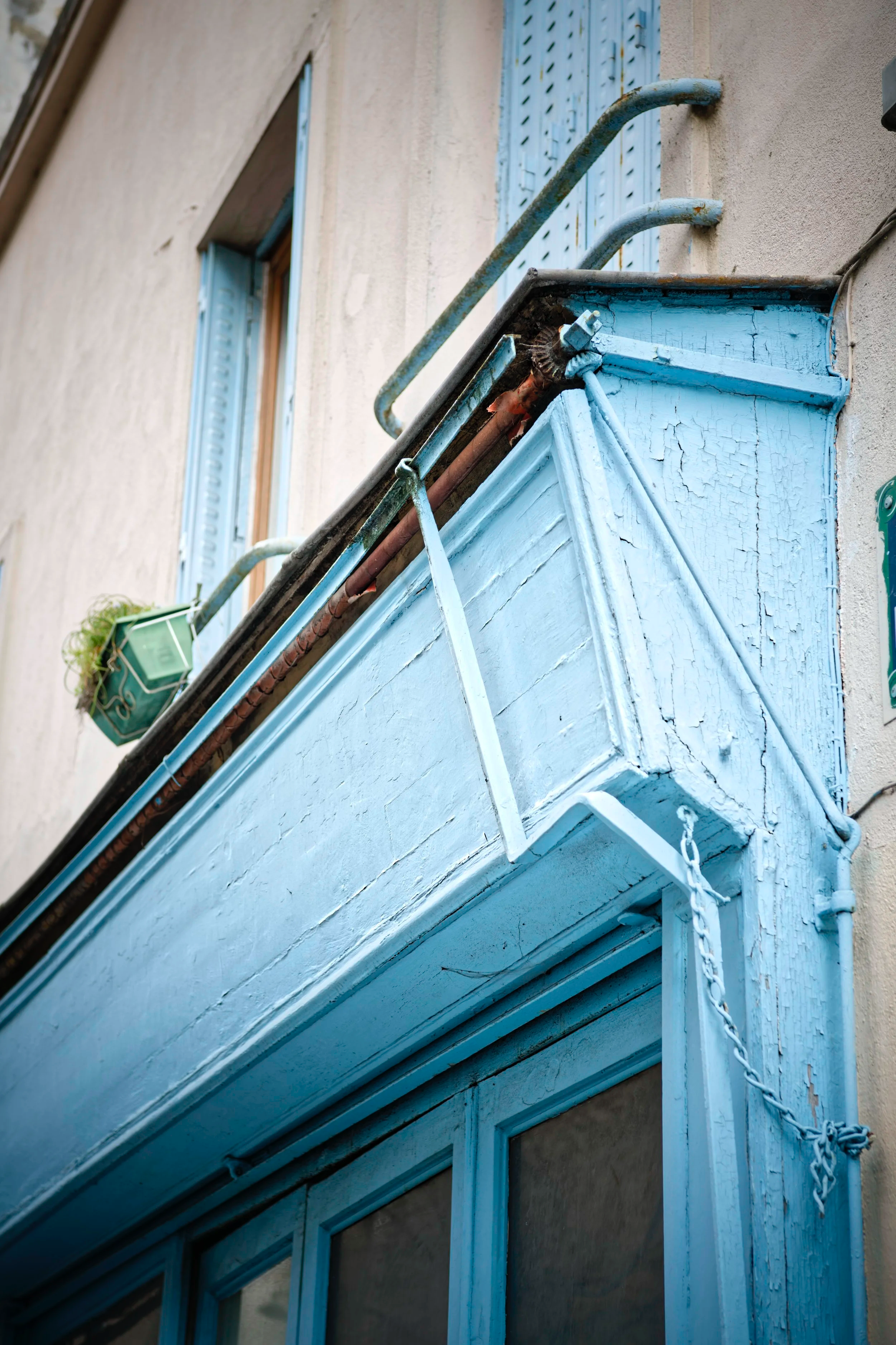 Close-up of a weathered blue balcony with peeling paint and rusted metal railings on an aging building exterior.
