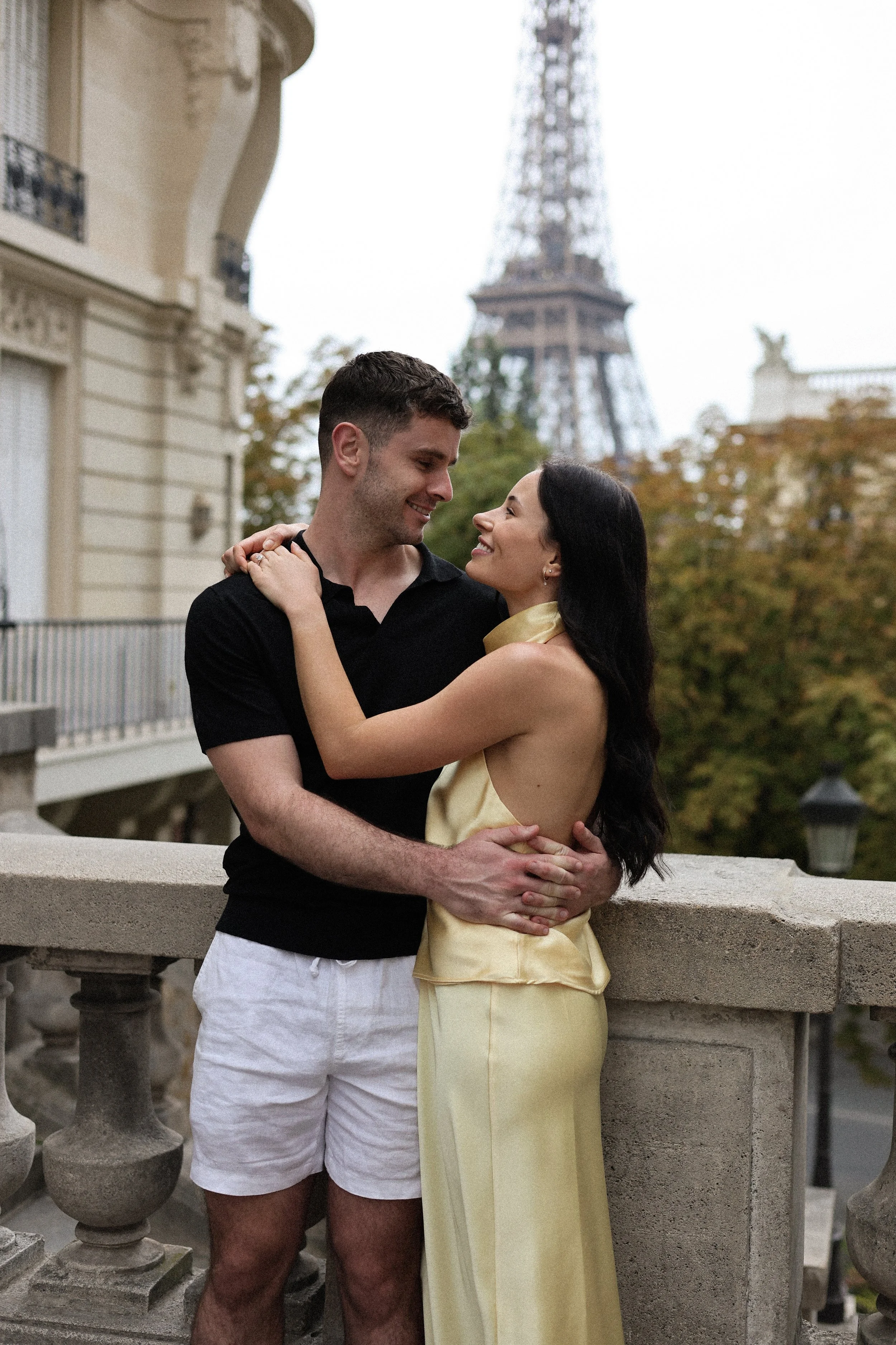 A couple embracing on a Paris balcony with the Eiffel Tower in the background, during daytime.
