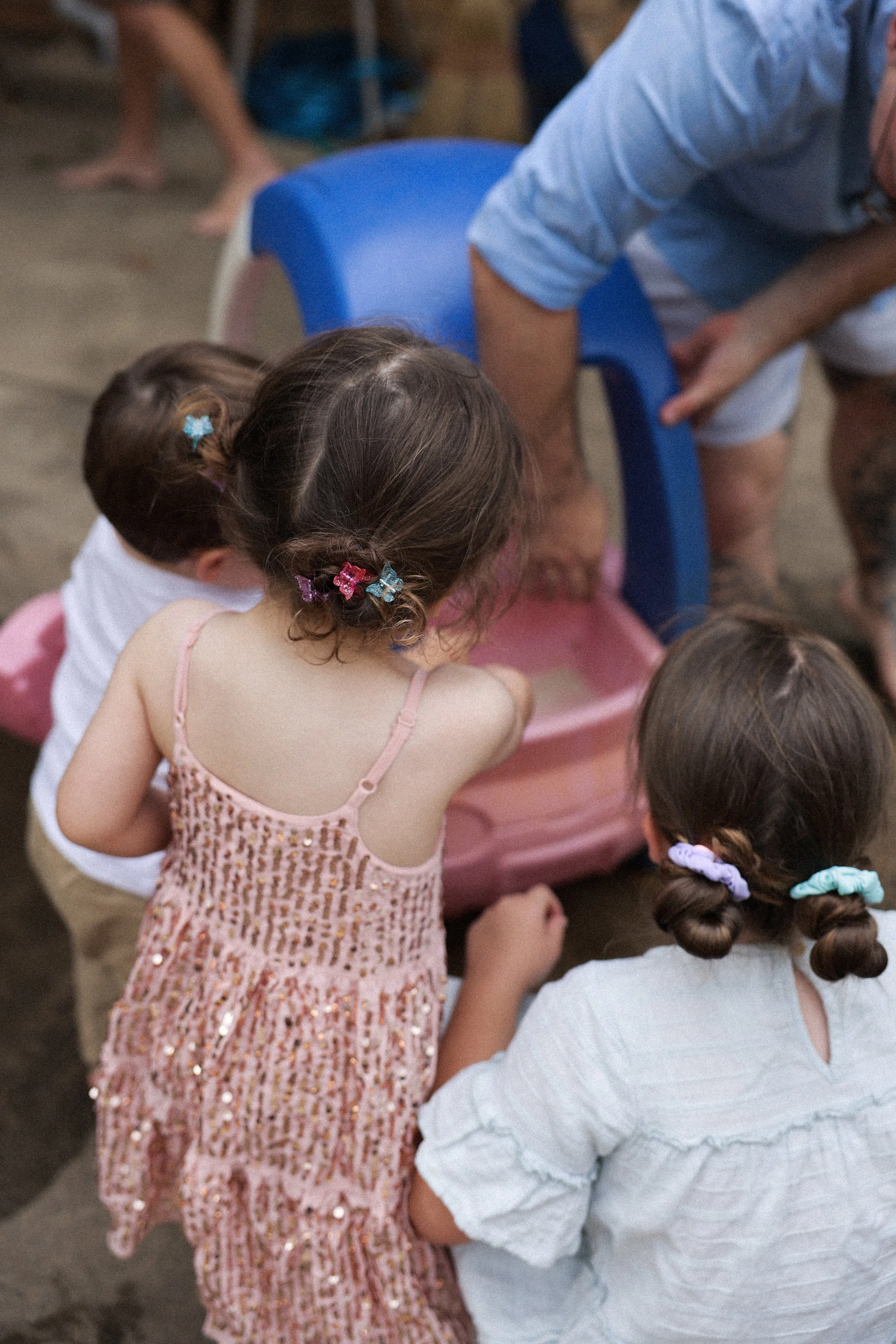 Children gathered around a pink sandpit, with an adult leaning over it, likely playing or supervising.