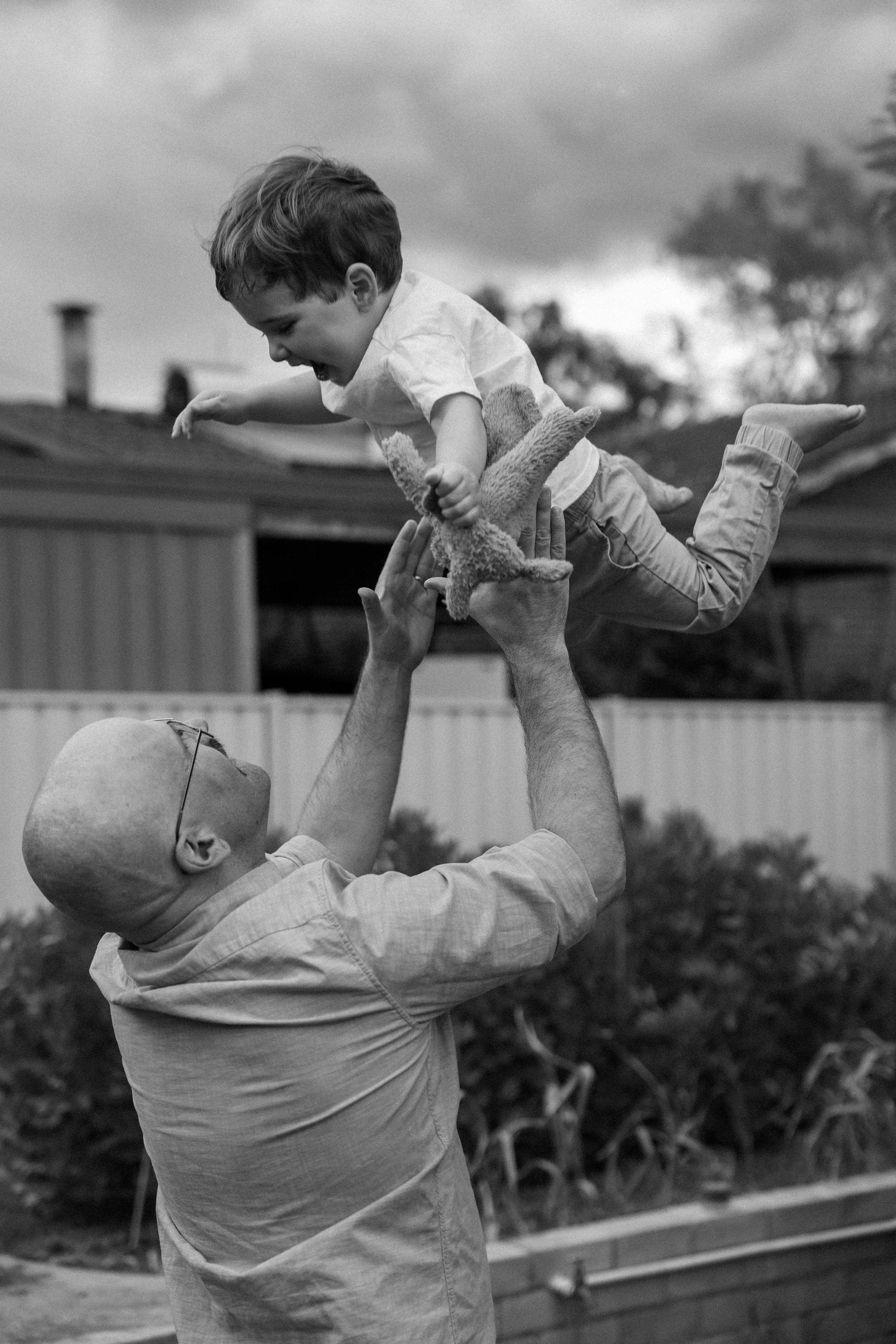 A man lifting a young boy in the air while playing outdoors, both smiling and enjoying themselves.