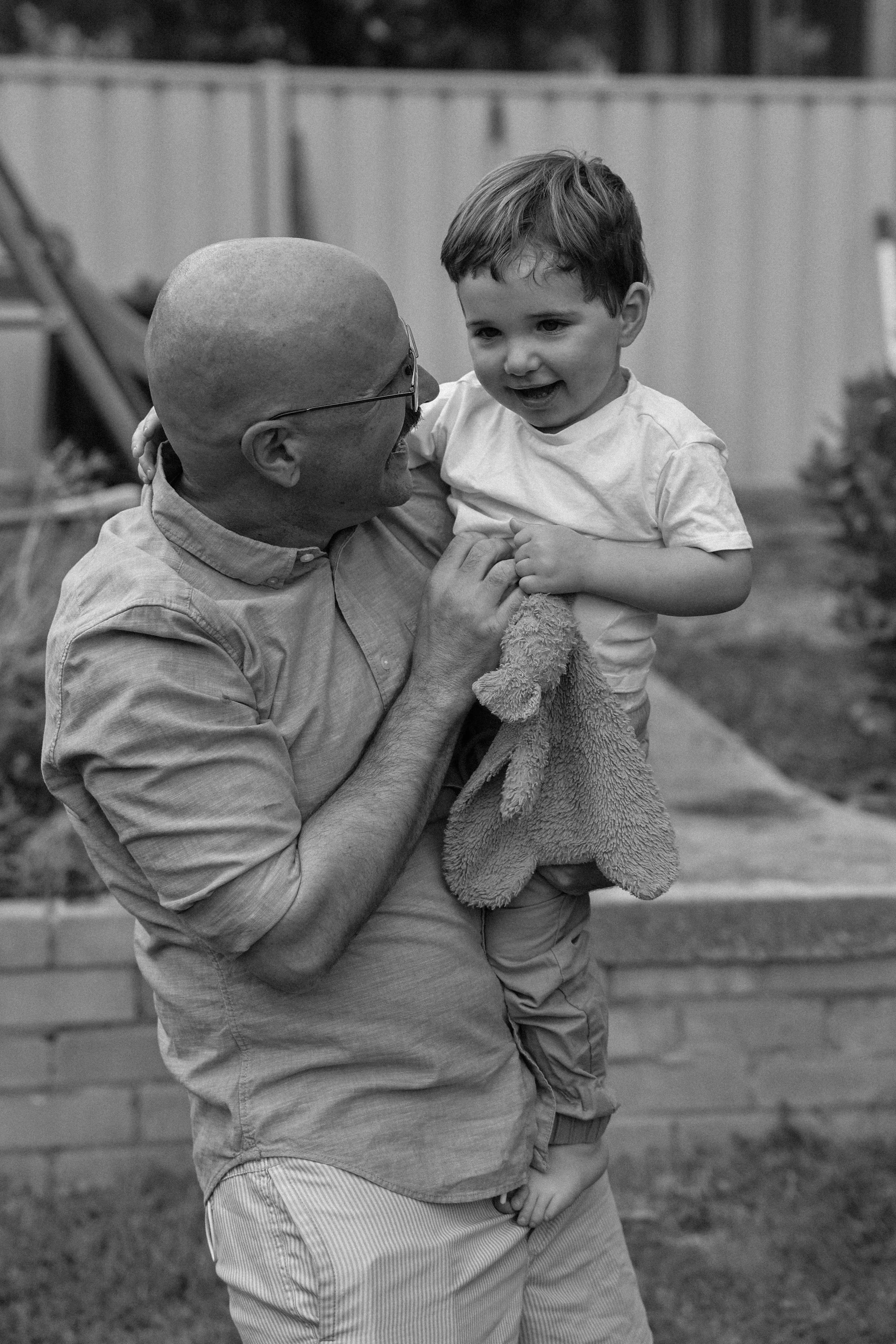A man holding a young boy, both smiling, outdoors in a backyard.