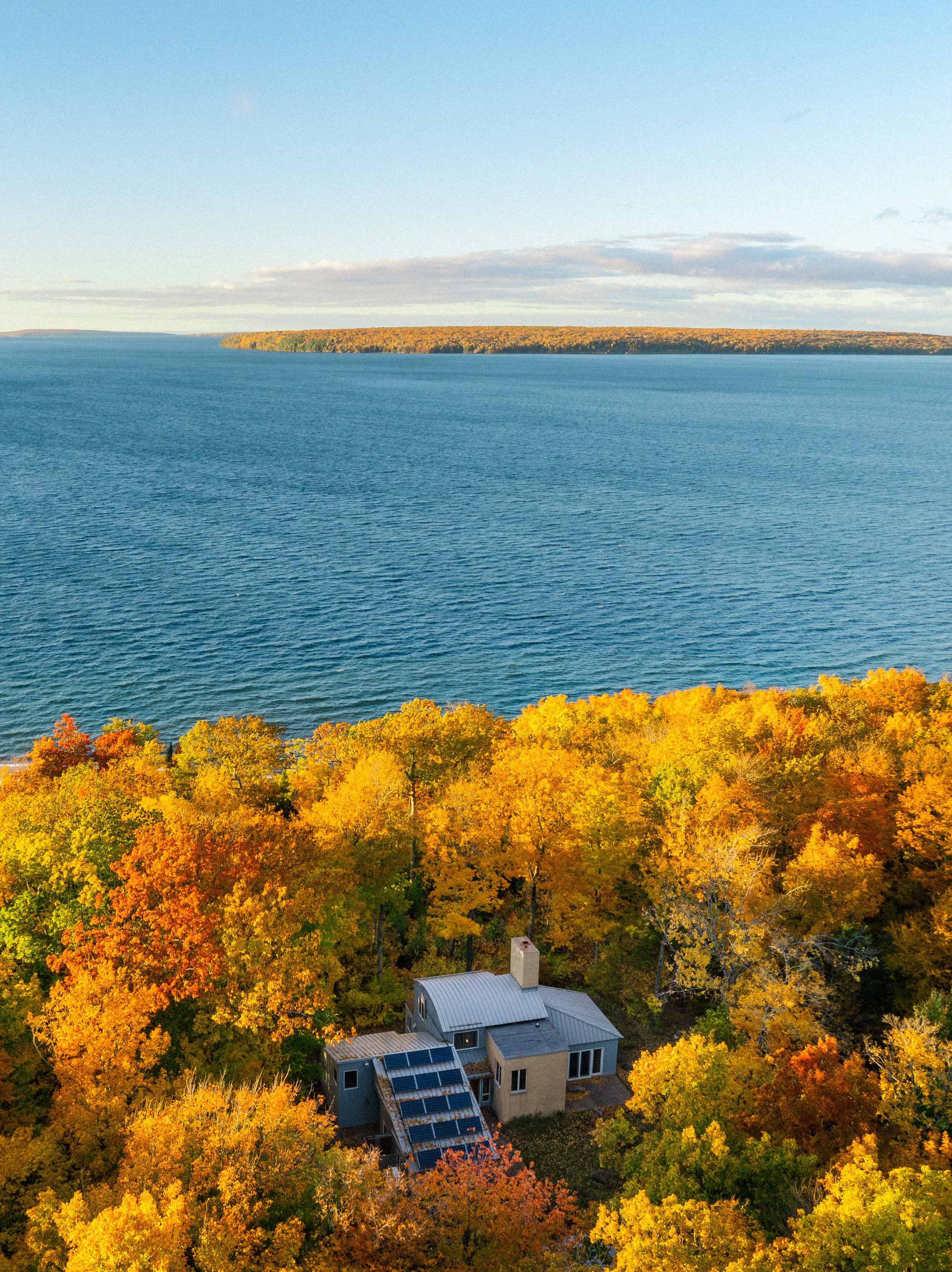 The Haven, boutique vacation rental, on Madeline Island with solar panels on the roof surrounded by colorful autumn trees near Lake Superior under a clear sky.