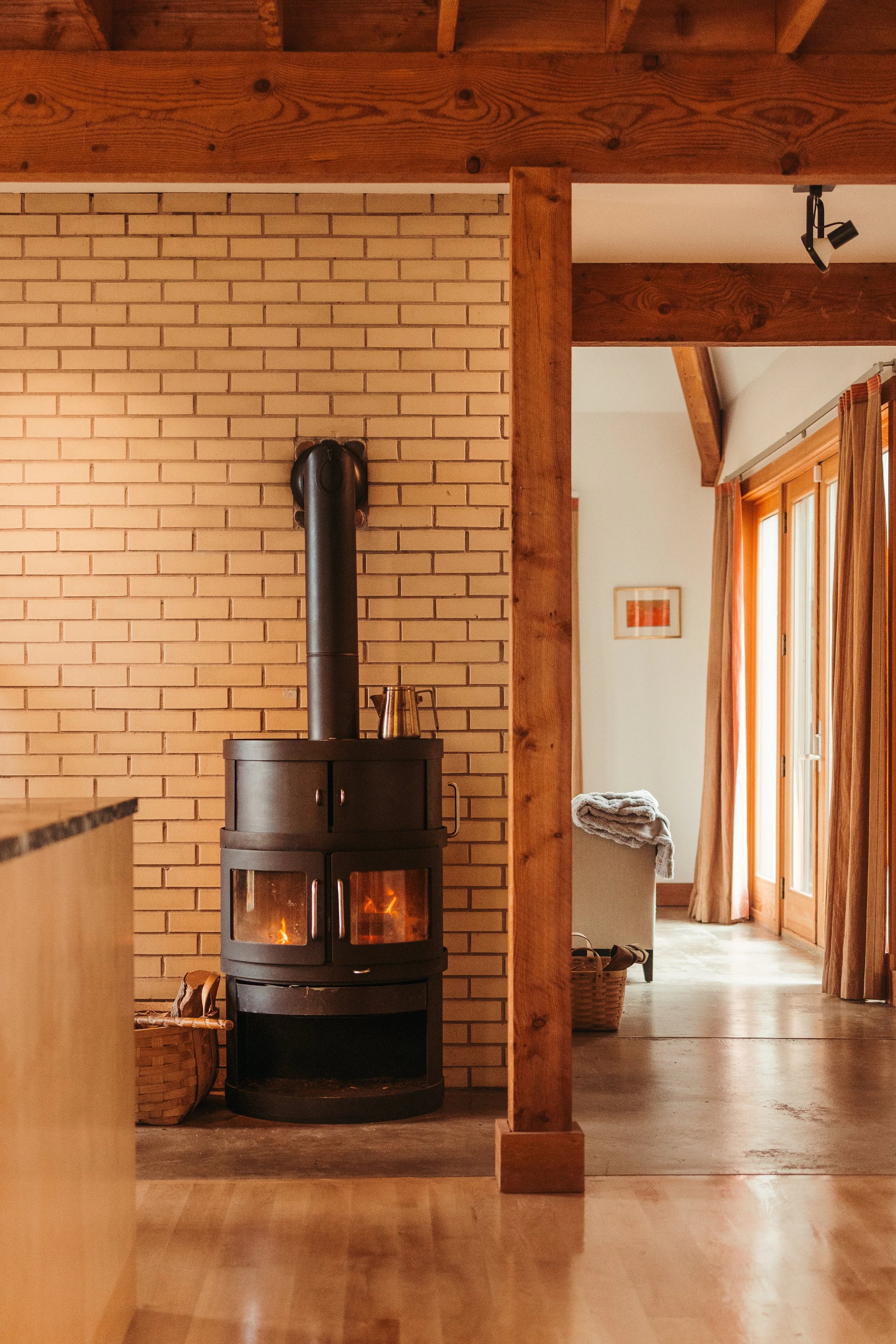 A cozy interior featuring a black wood stove with a glowing fire, against a brick wall, with a basket of firewood nearby.