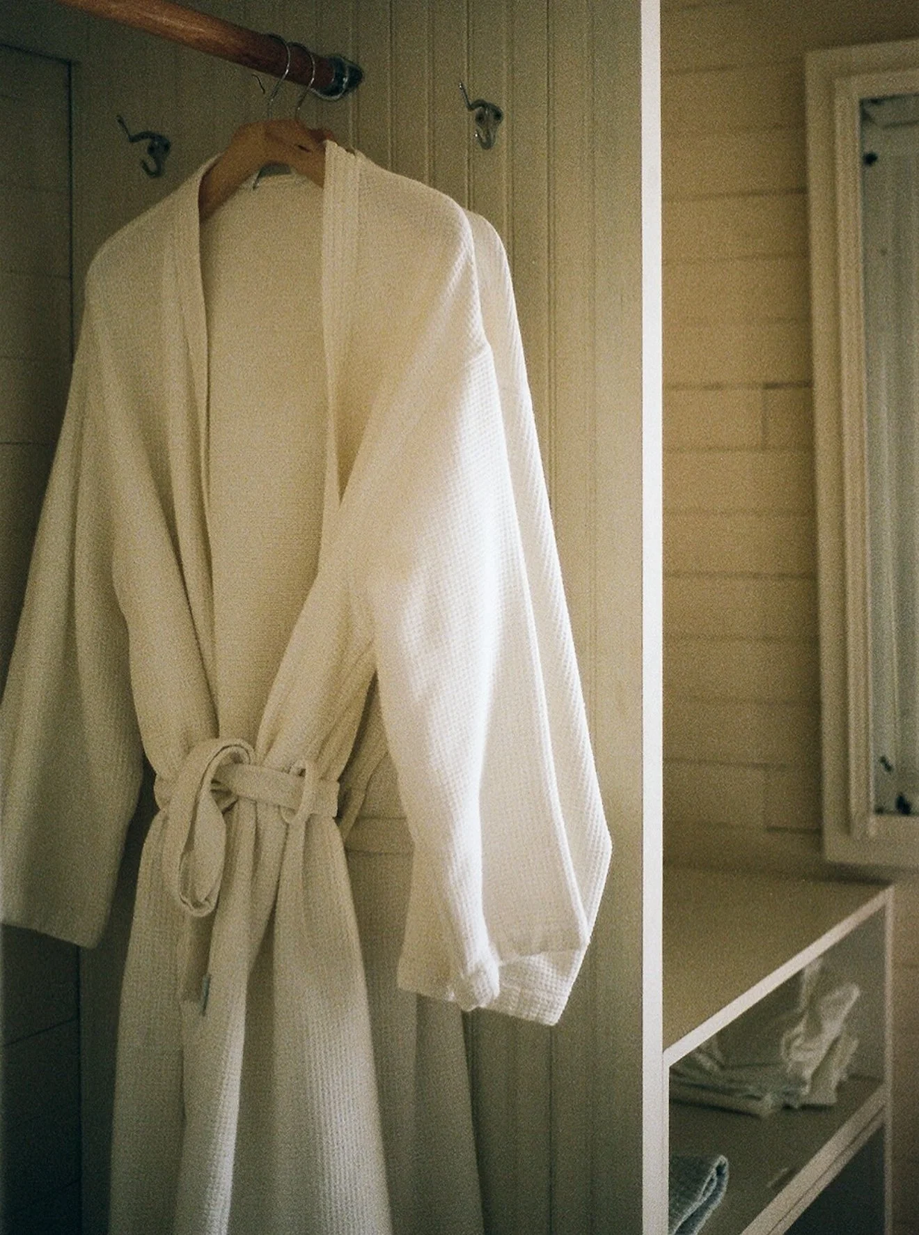 A white bathrobe hanging on a wooden hanger in a closet.