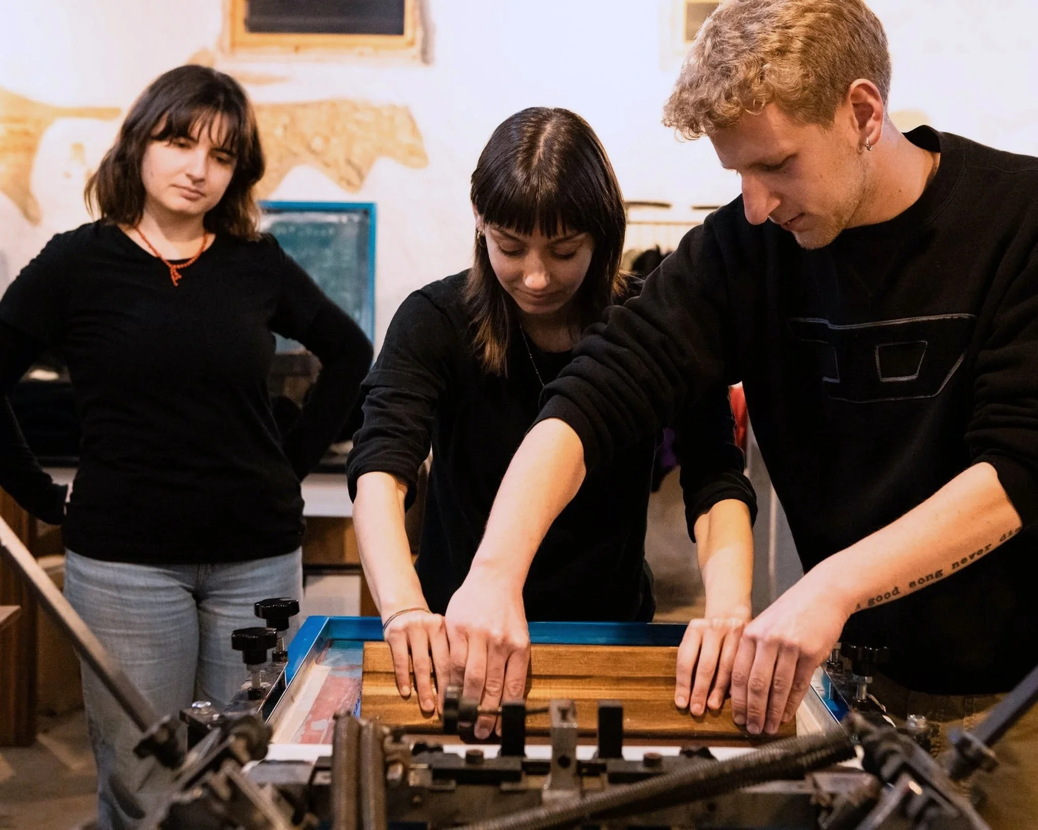 Due persone stanno serigrafando movendo la racla, mentre una terza osserva il processo.