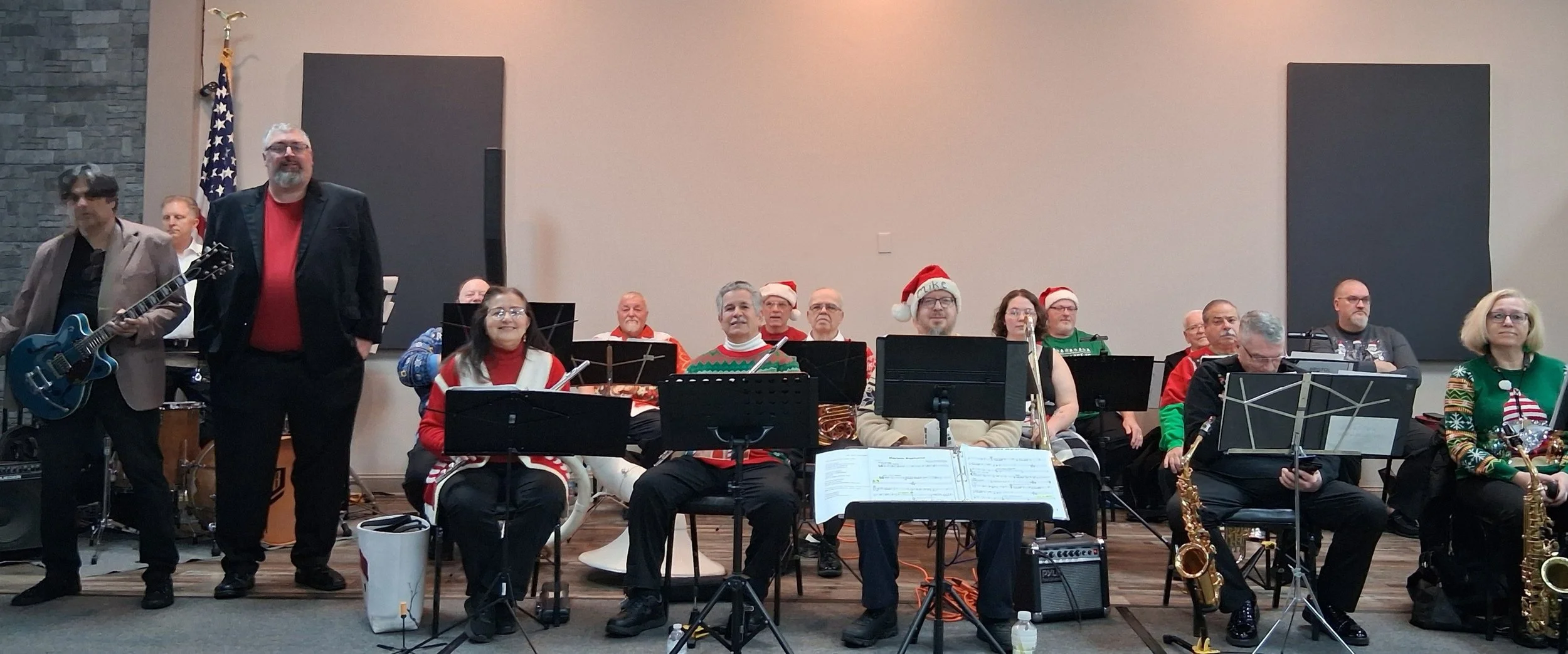 A group of musicians performing on stage during a Christmas concert, with some wearing Santa hats and Christmas sweaters.