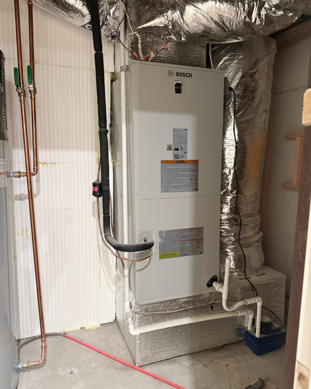 HVAC system installed in a basement utility room with copper, black insulated, and white PEX piping, with insulation and electrical wiring visible.
