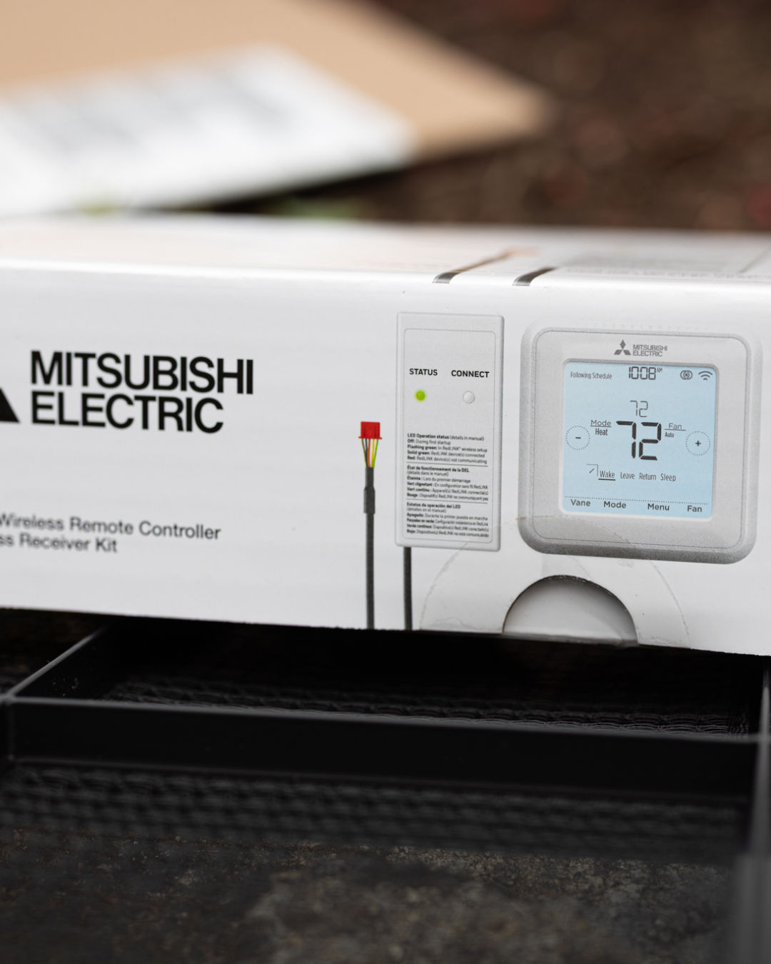 Close-up of a Mitsubishi Electric wireless remote control thermostat display showing a temperature of 72°F, with additional controls and status indicators, in front of its packaging box.