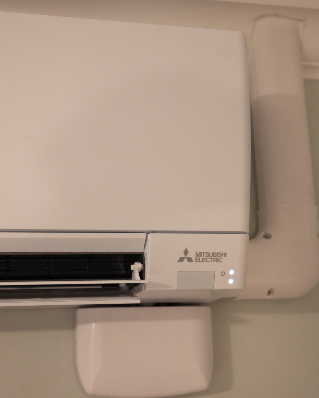 Close-up view of a Mitsubishi Electric air conditioning unit mounted on a wall, with two indicator lights illuminated.