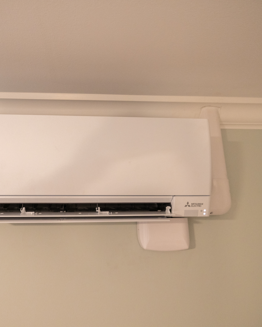 Close-up of a white Mitsubishi Electric air conditioning unit installed on a ceiling with beige walls.