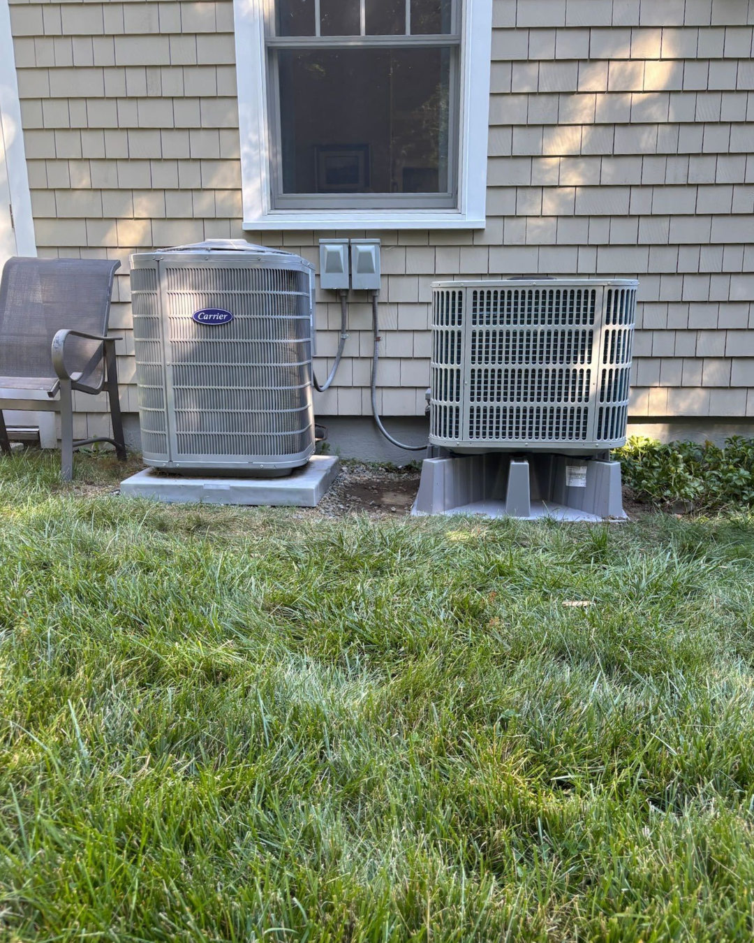 An outdoor scene with a bench on the left, two air conditioning units, a window above, and green grass in the foreground.