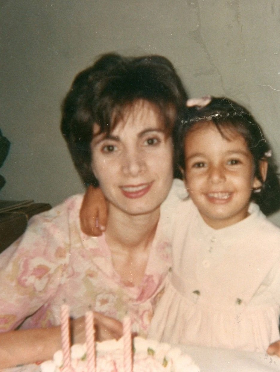 A woman and a young girl smiling and embracing each other at a celebration with a birthday cake in front of them.