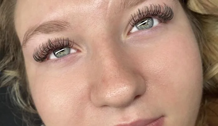 Close-up of a woman's face focusing on her eyes, showcasing long eyelashes and light-colored eye makeup.