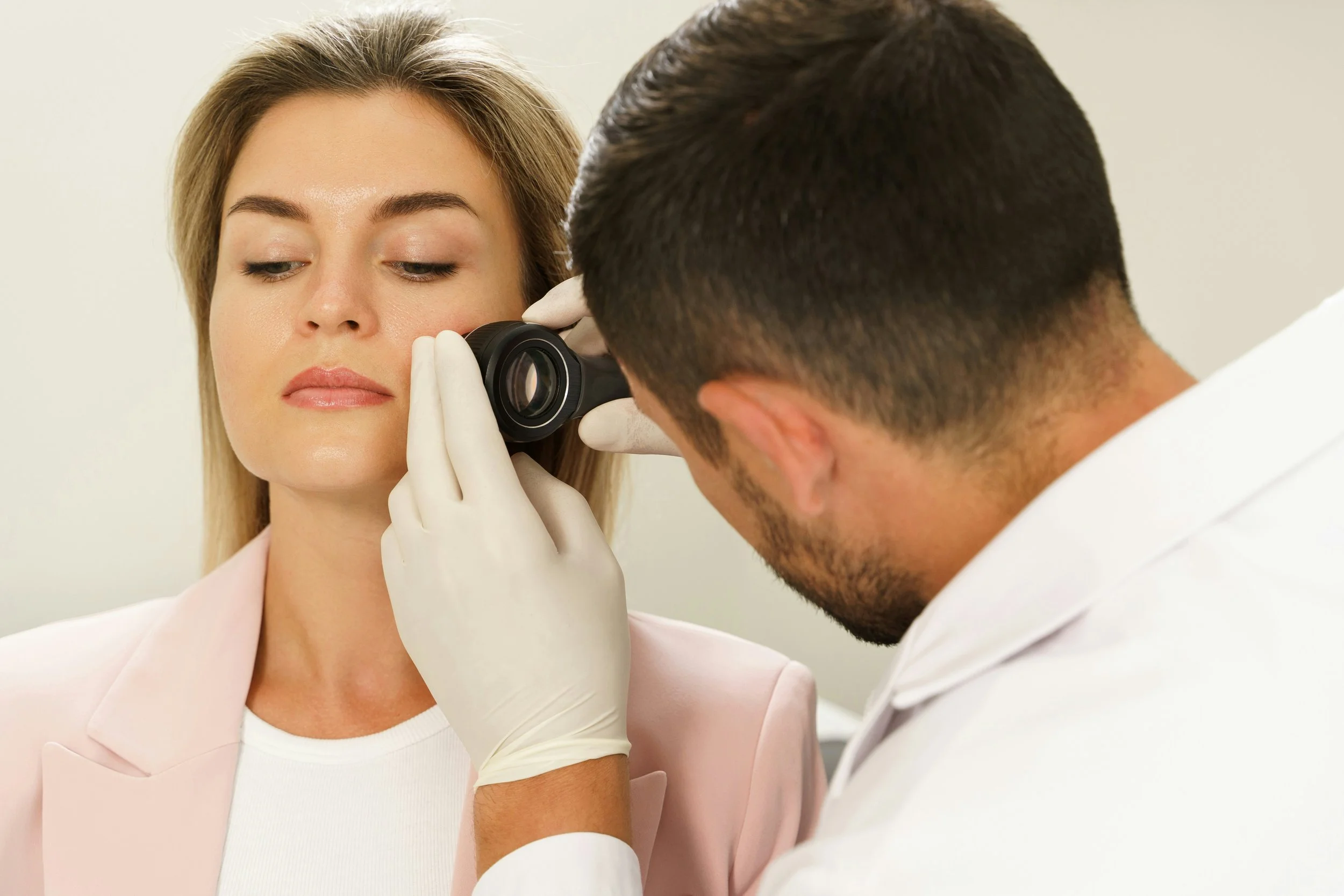 A doctor examines a woman's skin using a dermatoscope.