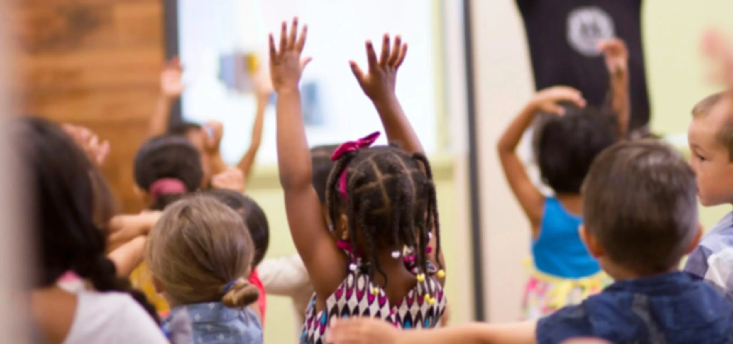 Children in a classroom raising their hands to answer a question.