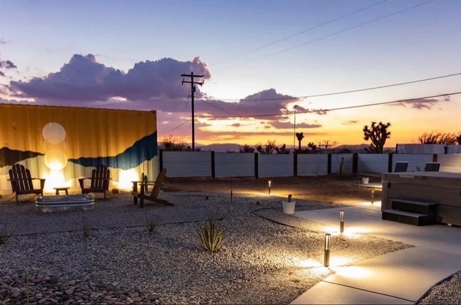Outdoor patio in desert landscape at sunset with seating area, firepit, and decorative landscape lighting.