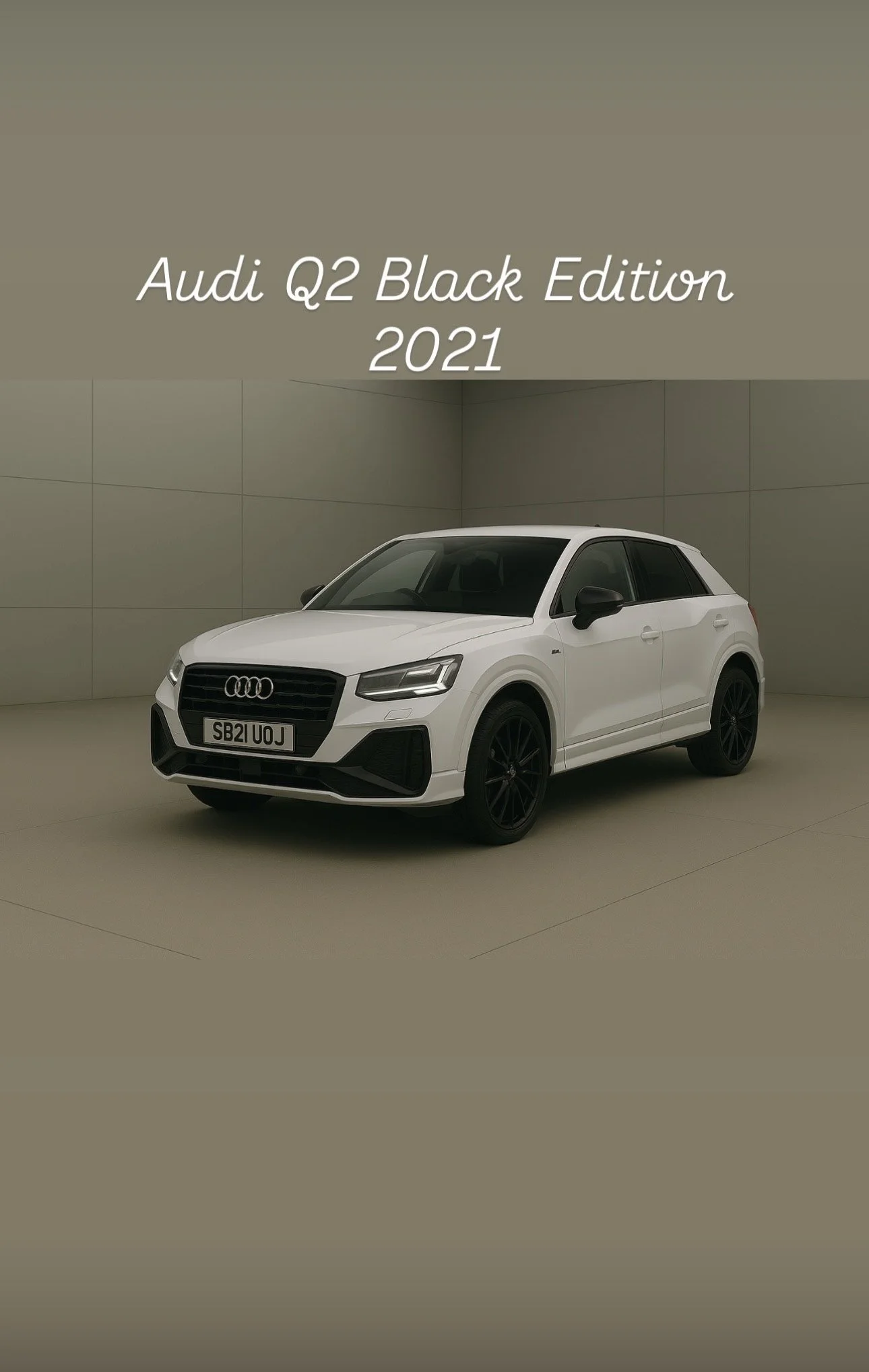 A white 2021 Audi Q2 Black Edition parked in an indoor showroom with beige walls. The car has black wheels and black side mirrors, with the Audi logo visible on the front grille.