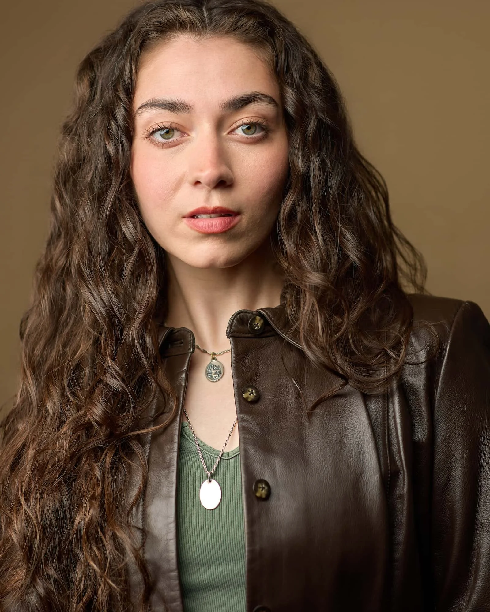 Theatrical headshot of a female actress wearing a green shirt and brown leather jacket