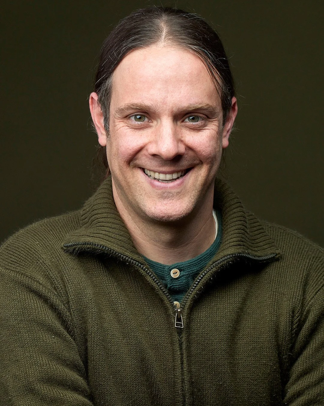 Acting headshot of a man wearing a green sweater with a green backdrop