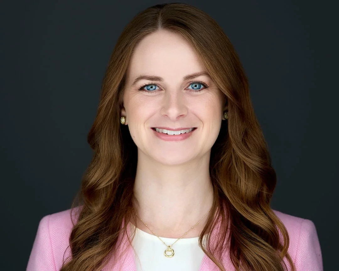 Headshot of a female with brown hair, blue eyes wearing a pink blazer and white shirt for her linkedin profile