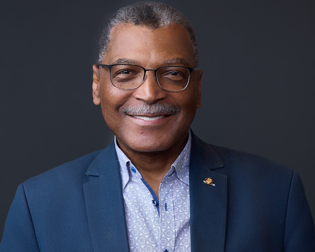 Headshot of an african american man wearing glasses and a blue suit.