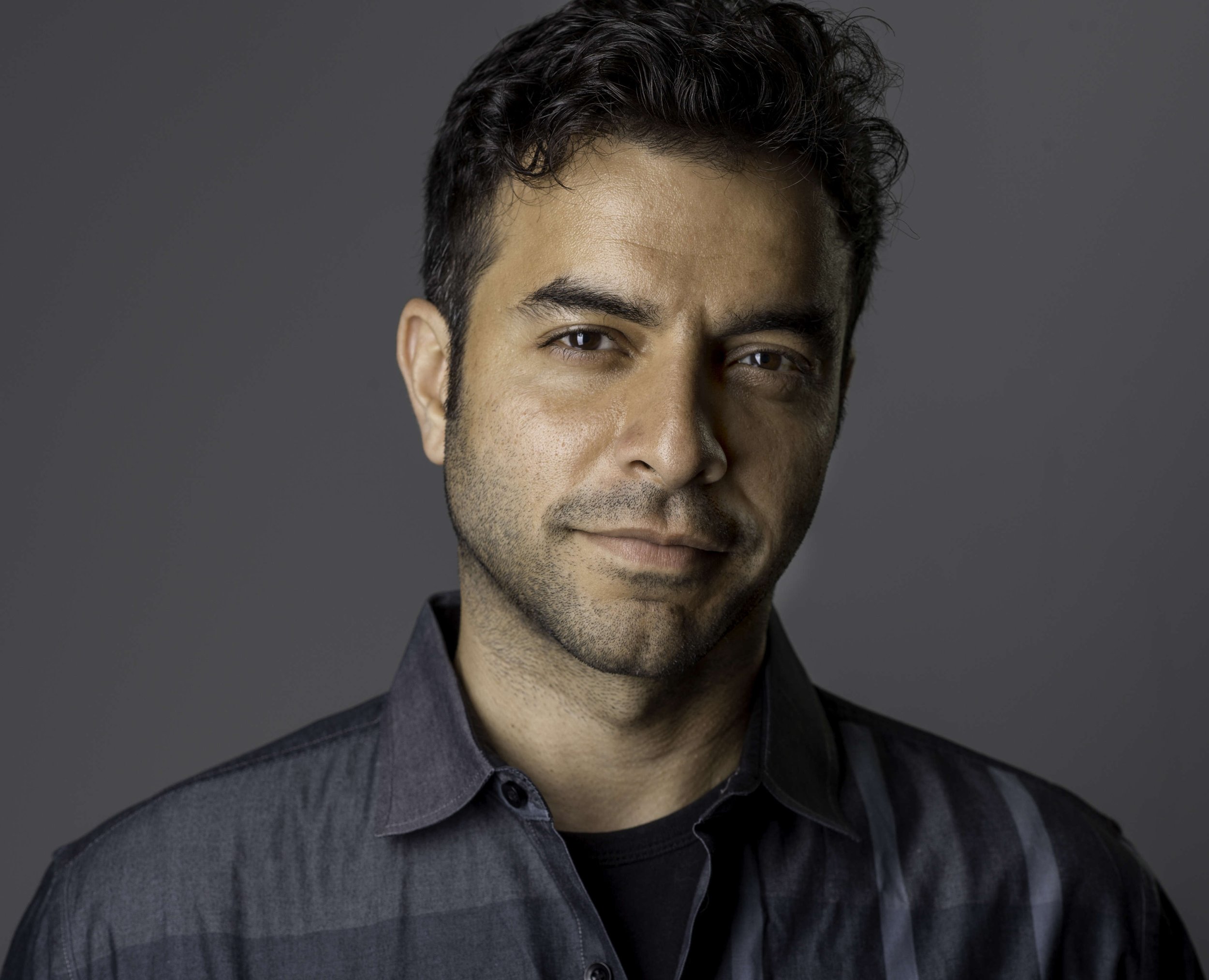 Portrait of a man with short dark hair and a subtle smile, wearing a dark collared shirt.
