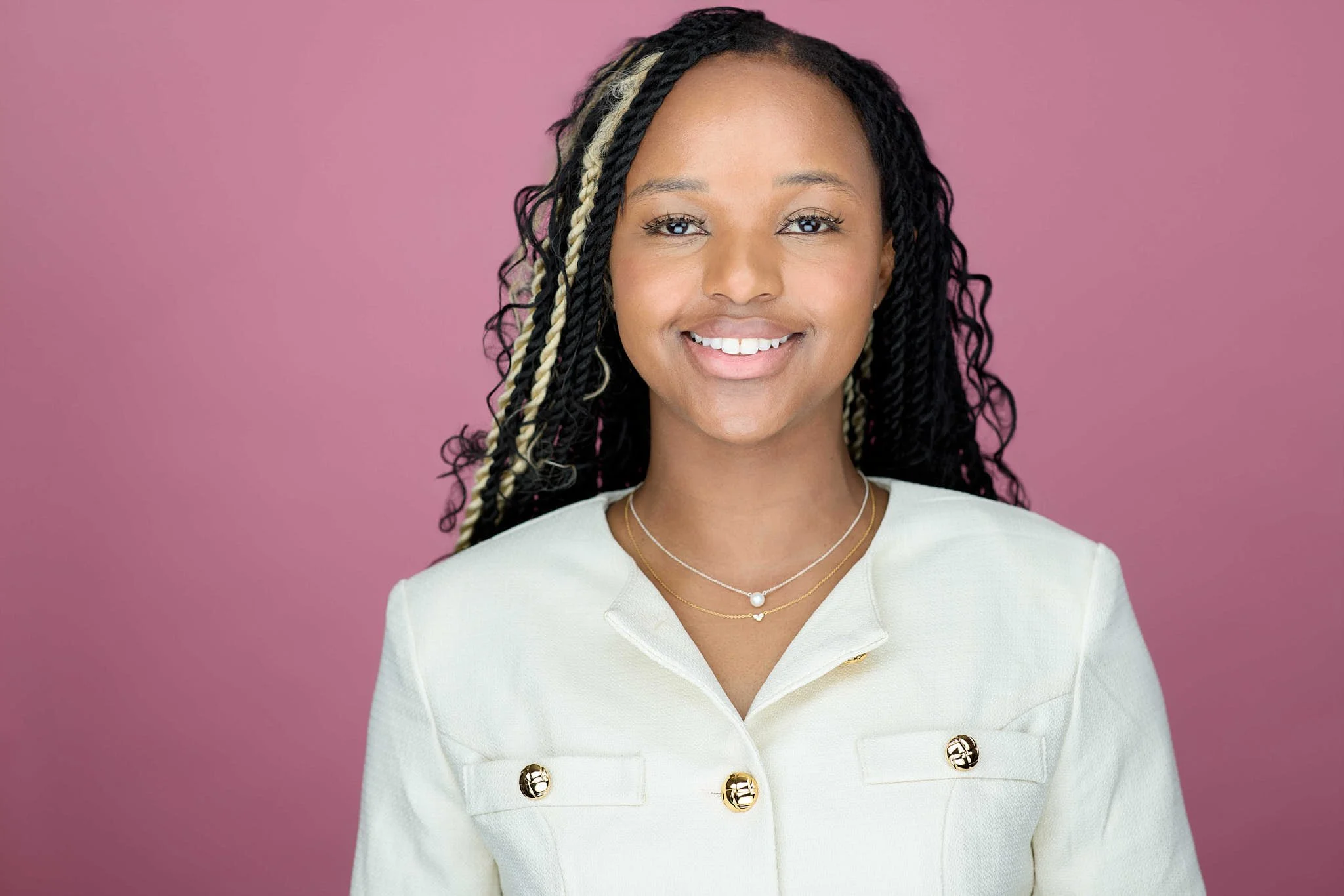 Linkedin Headshot of a woman wearing a white coat shot against a pink backdrop
