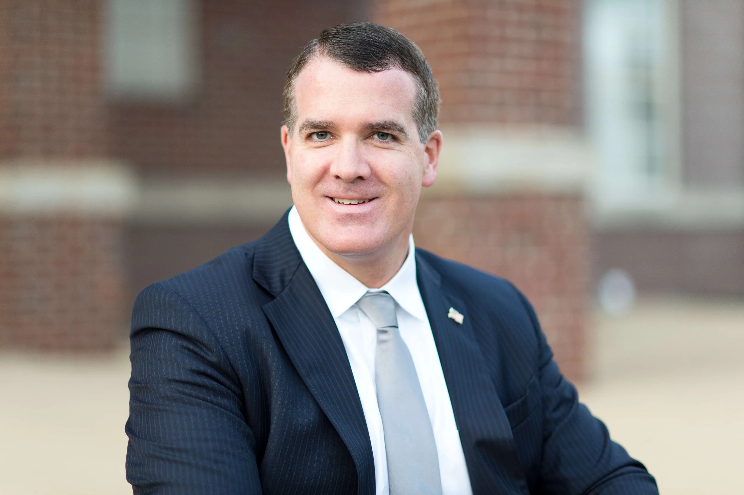 Man in a suit with a brick wall background.