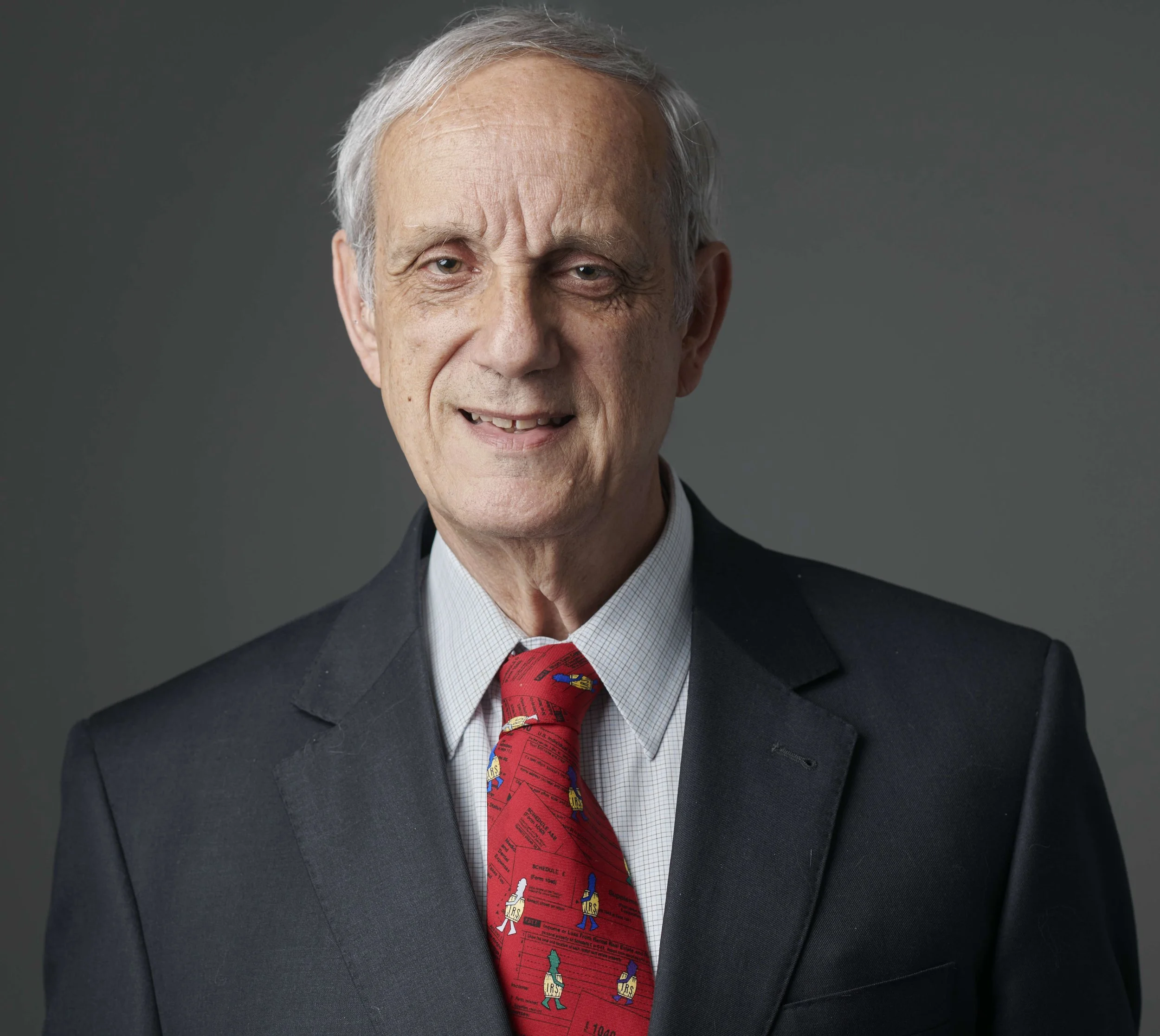 Elderly man in a suit and red tie with cartoons, smiling, gray background.
