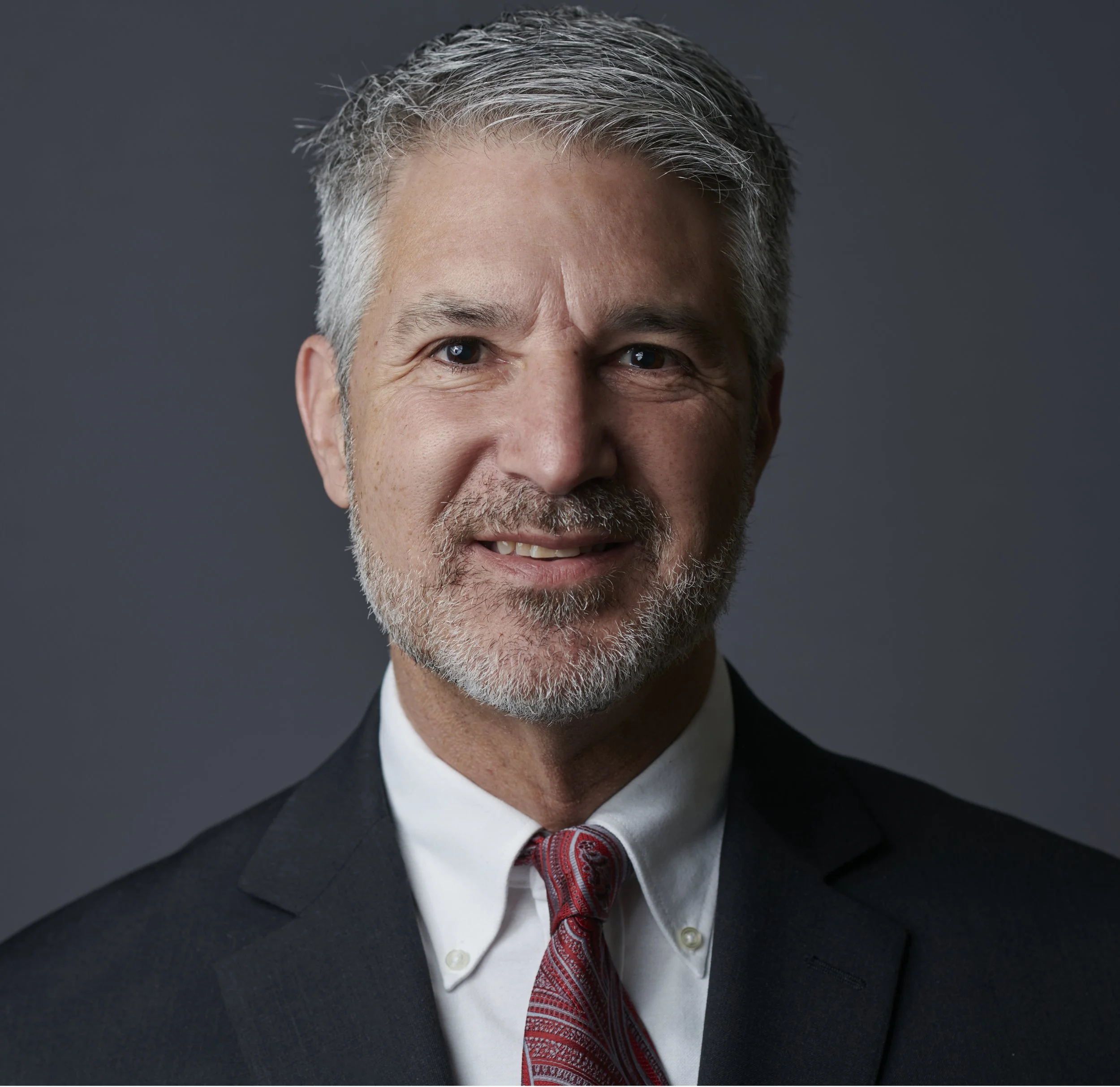 Portrait of a man with gray hair and beard wearing a suit and red tie