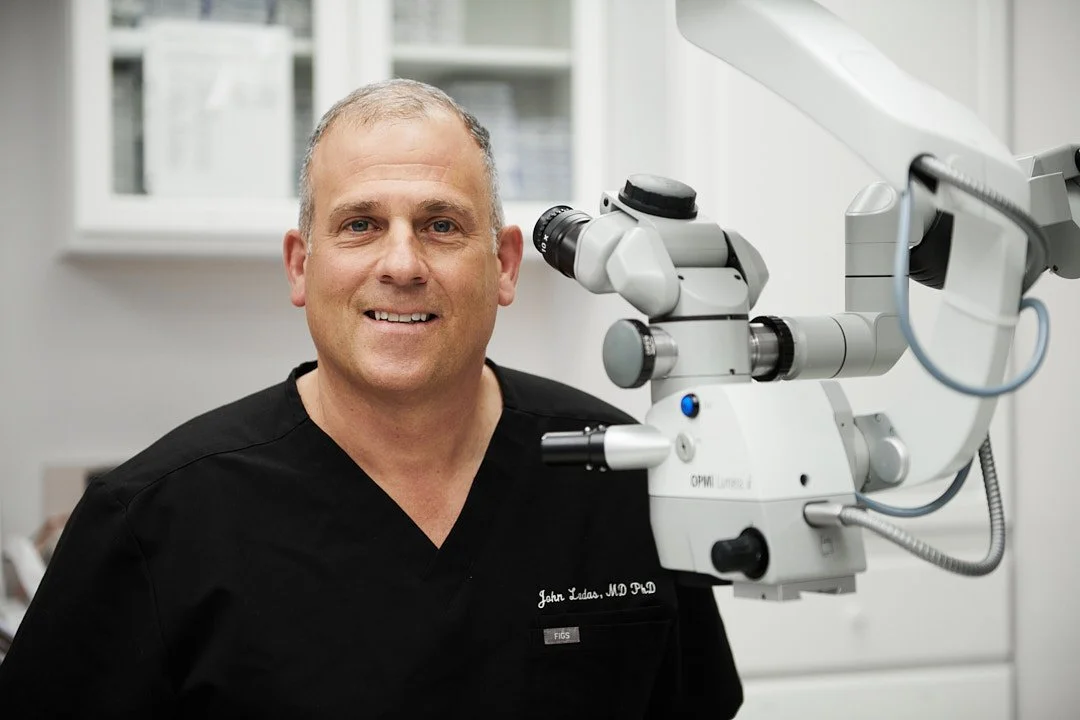 Portrait of an eye surgeon wearing black scrubs sitting at his microscope