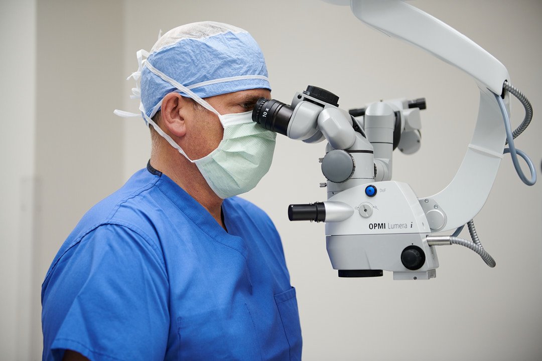 Branding portrait of an eye surgeon wearing blue scrubs, hat and mask with one of his surgical microscopes