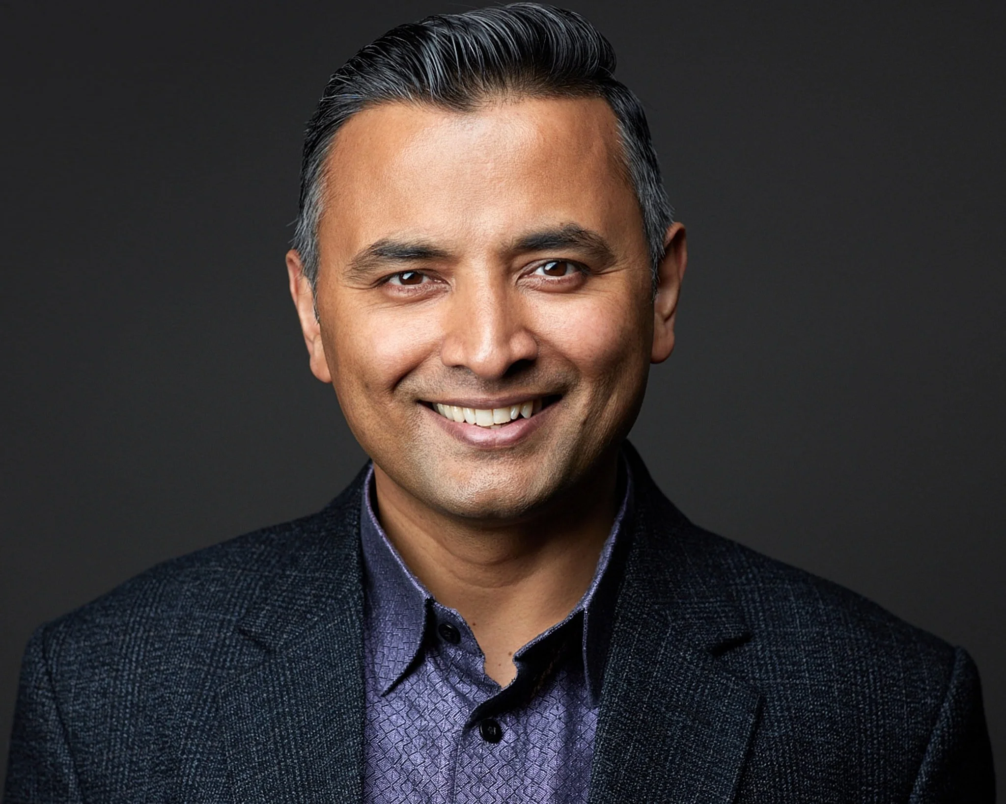 Headshot of a tech company CEO wearing a purple shirt and grey blazer