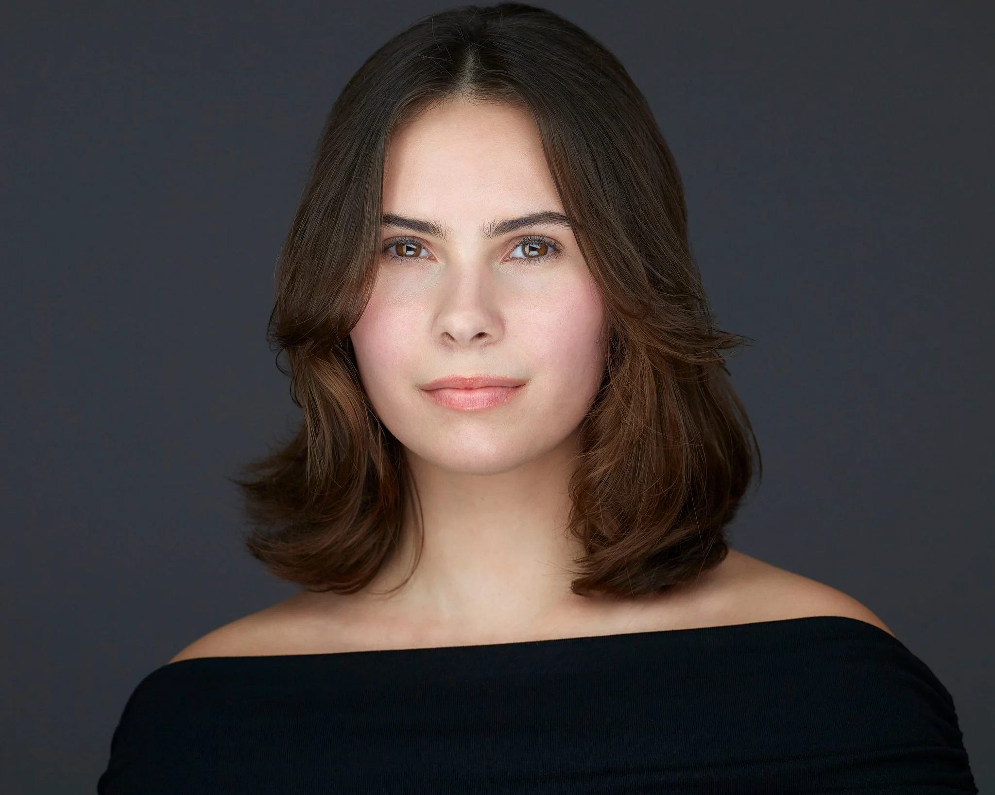 Headshot of a woman with brown hair and a neutral expression against a dark background.