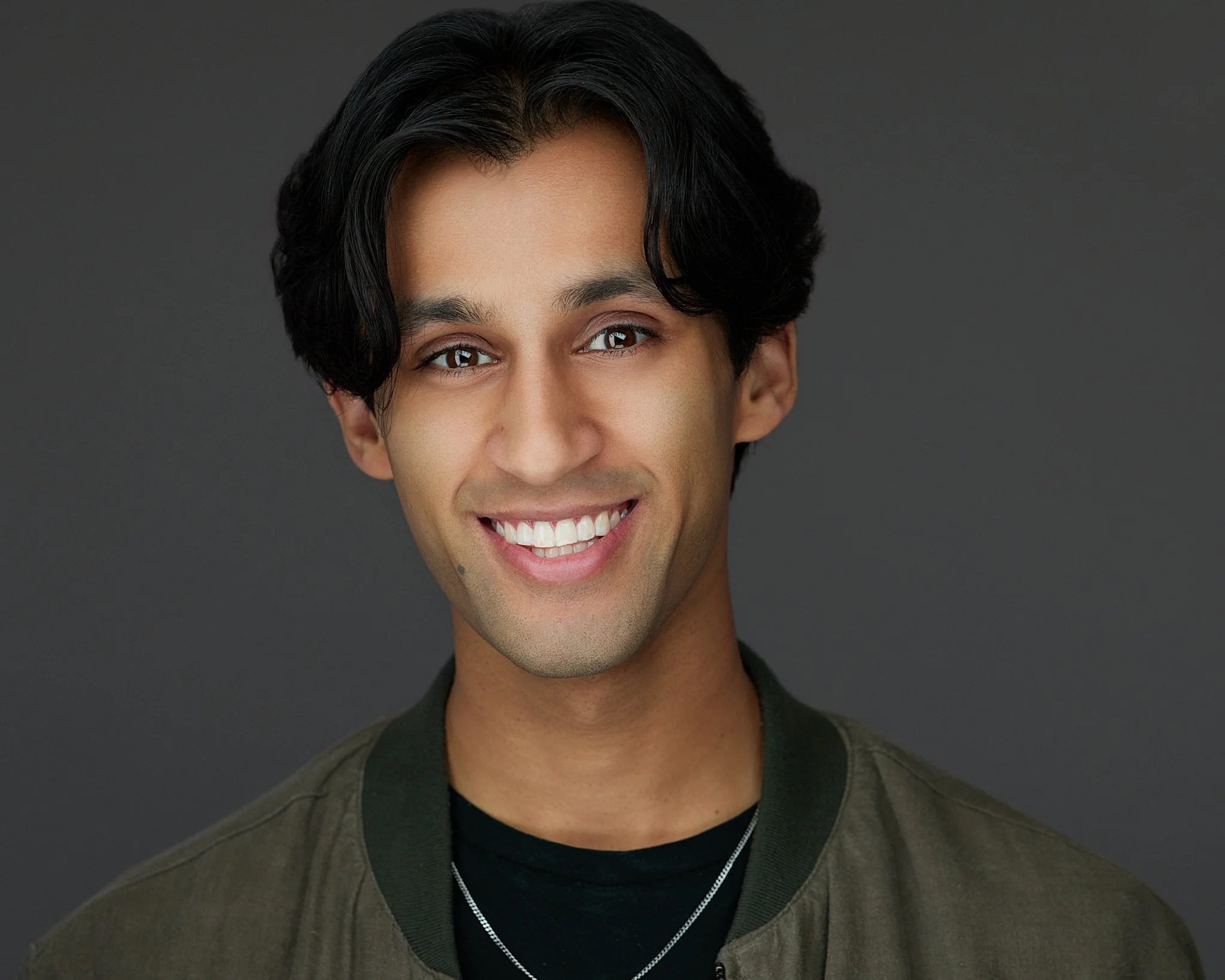Headshot of a male actor wearing a black shirt and green jacket