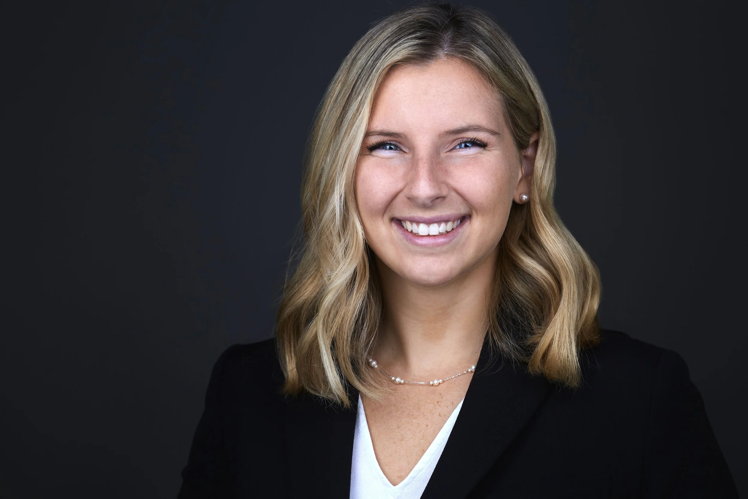 Professional Linkedin headshot of a female wearing a colorful hijab photographed against a greay backdrop.