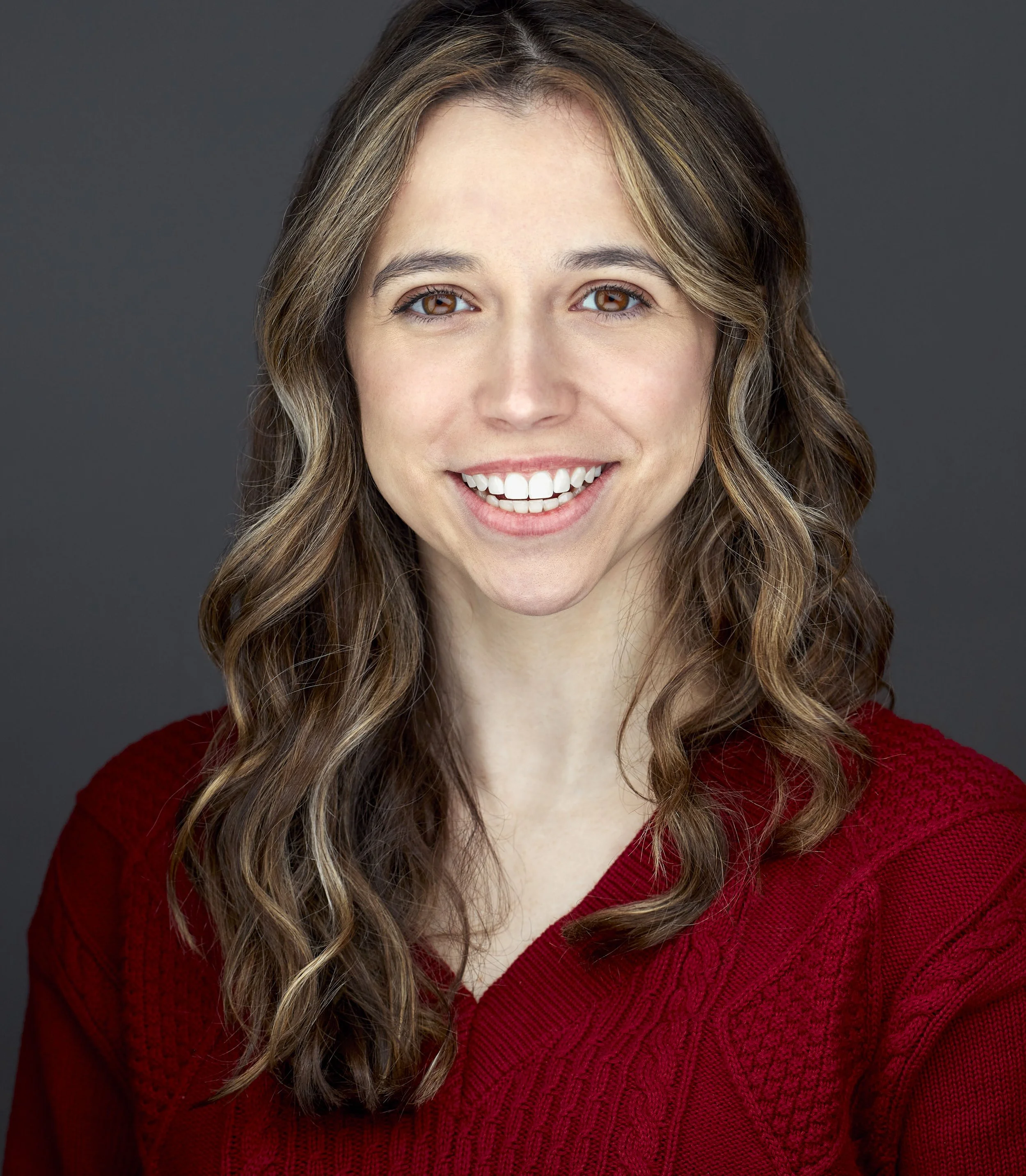 Headshot of a young female acress wearing a red sweater with long brown hair.