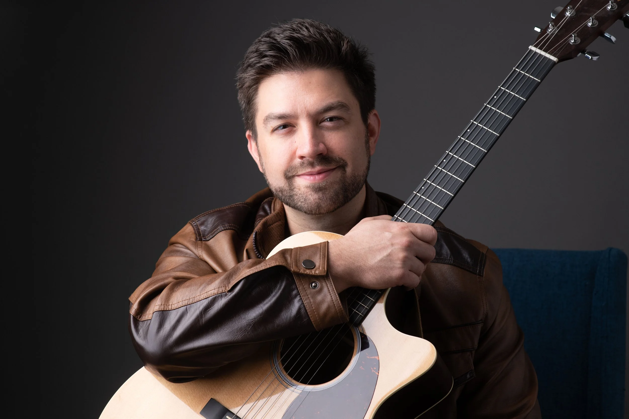 Man in brown leather jacket holding an acoustic guitar