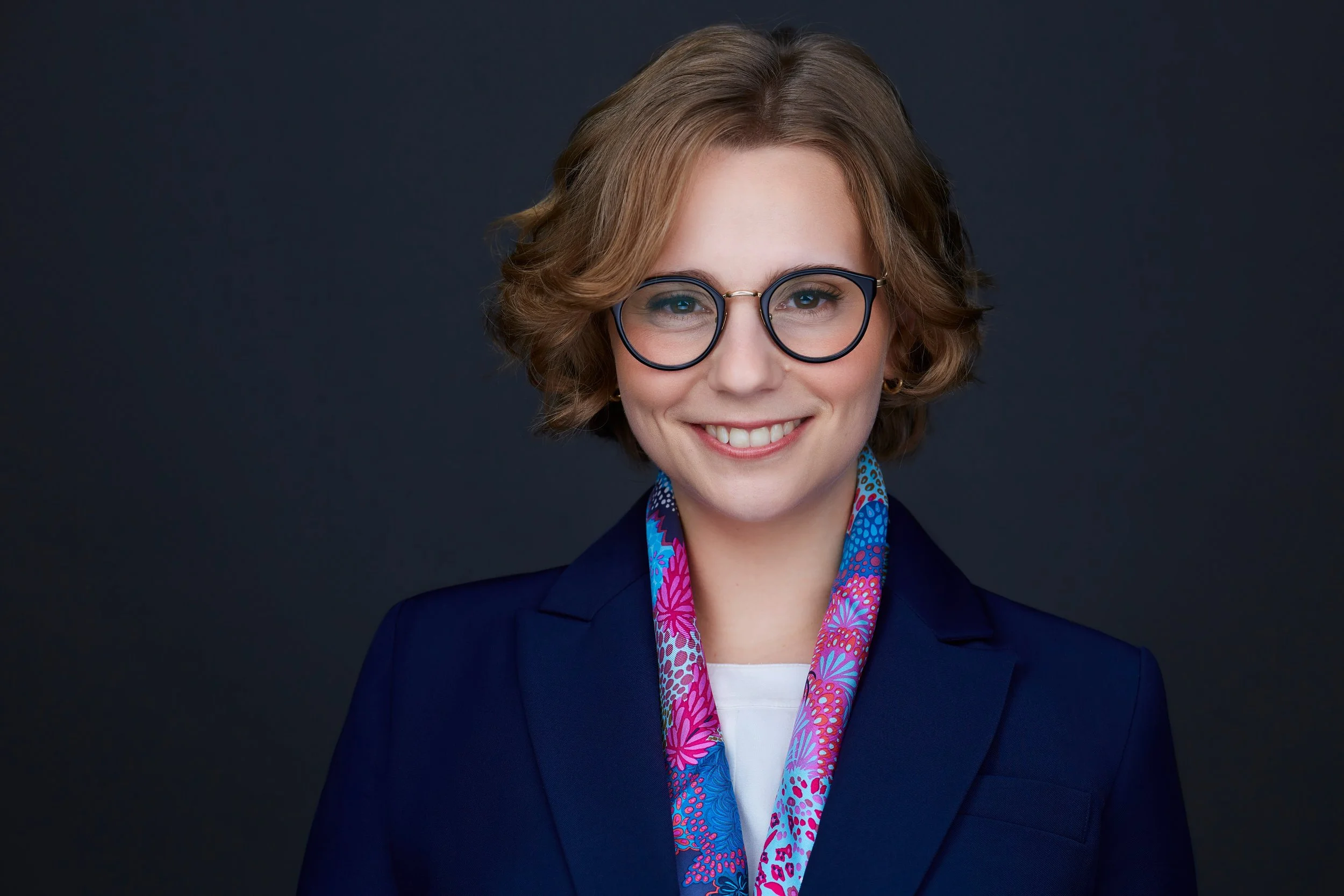 Headshot of a woman wearing a blue jacket and a colorful scarf
