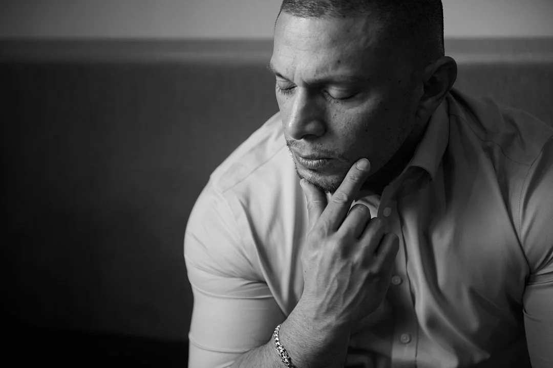 Black and white image of a man with short hair in a collared shirt, resting his chin on his hand with eyes closed, appearing thoughtful or contemplative.