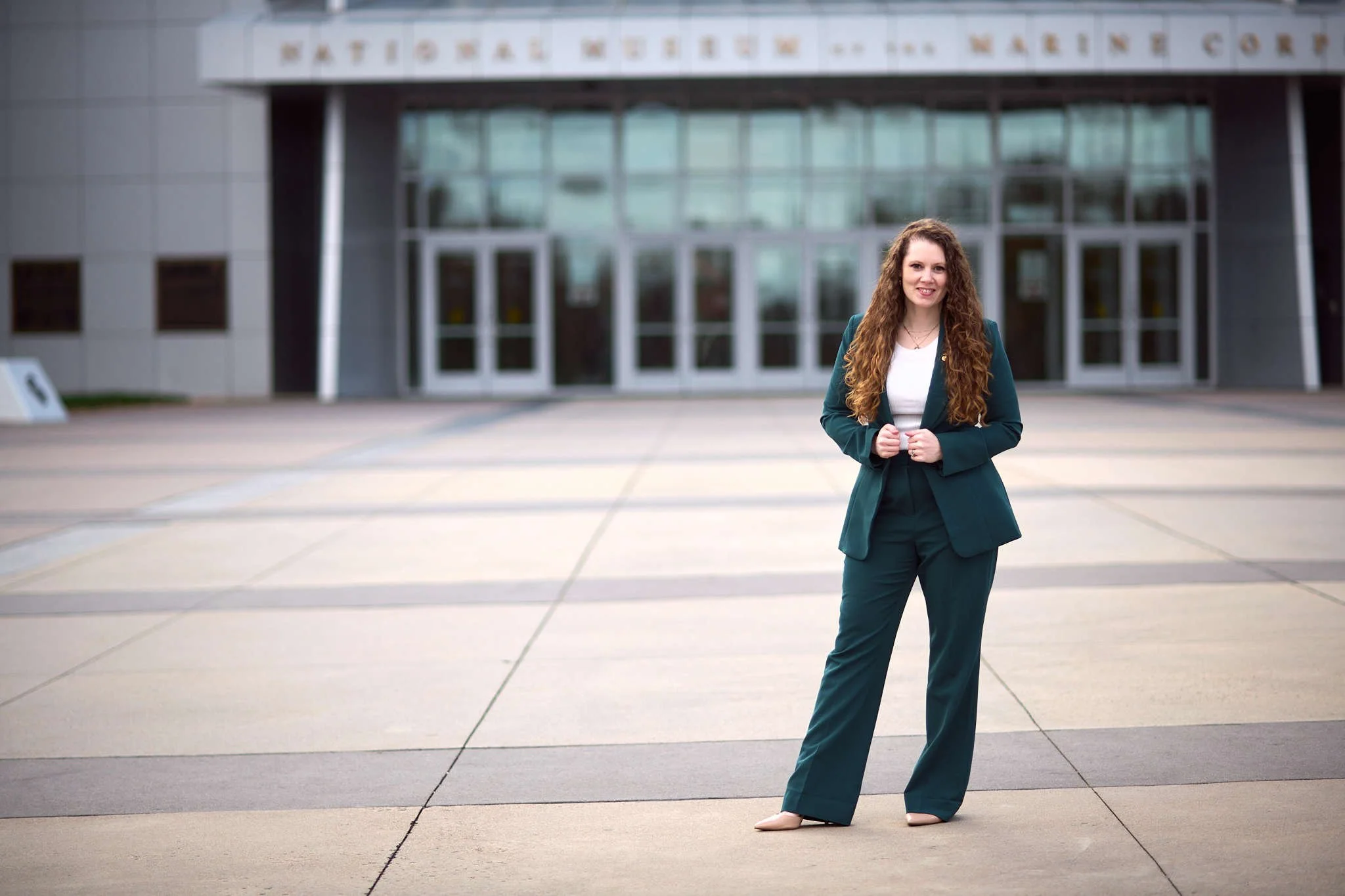 branding portrait of a woman in a green business suit standing outside a modern office building with glass doors.