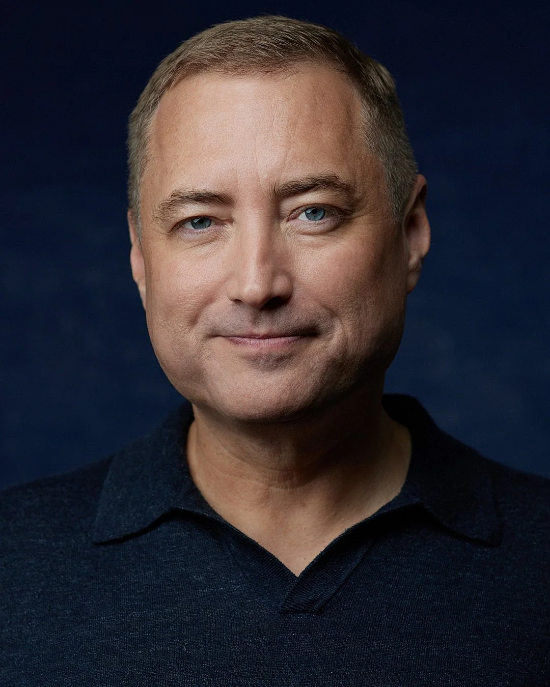 Professional headshot for an actor, make wearing blue shirt against a blue backdrop