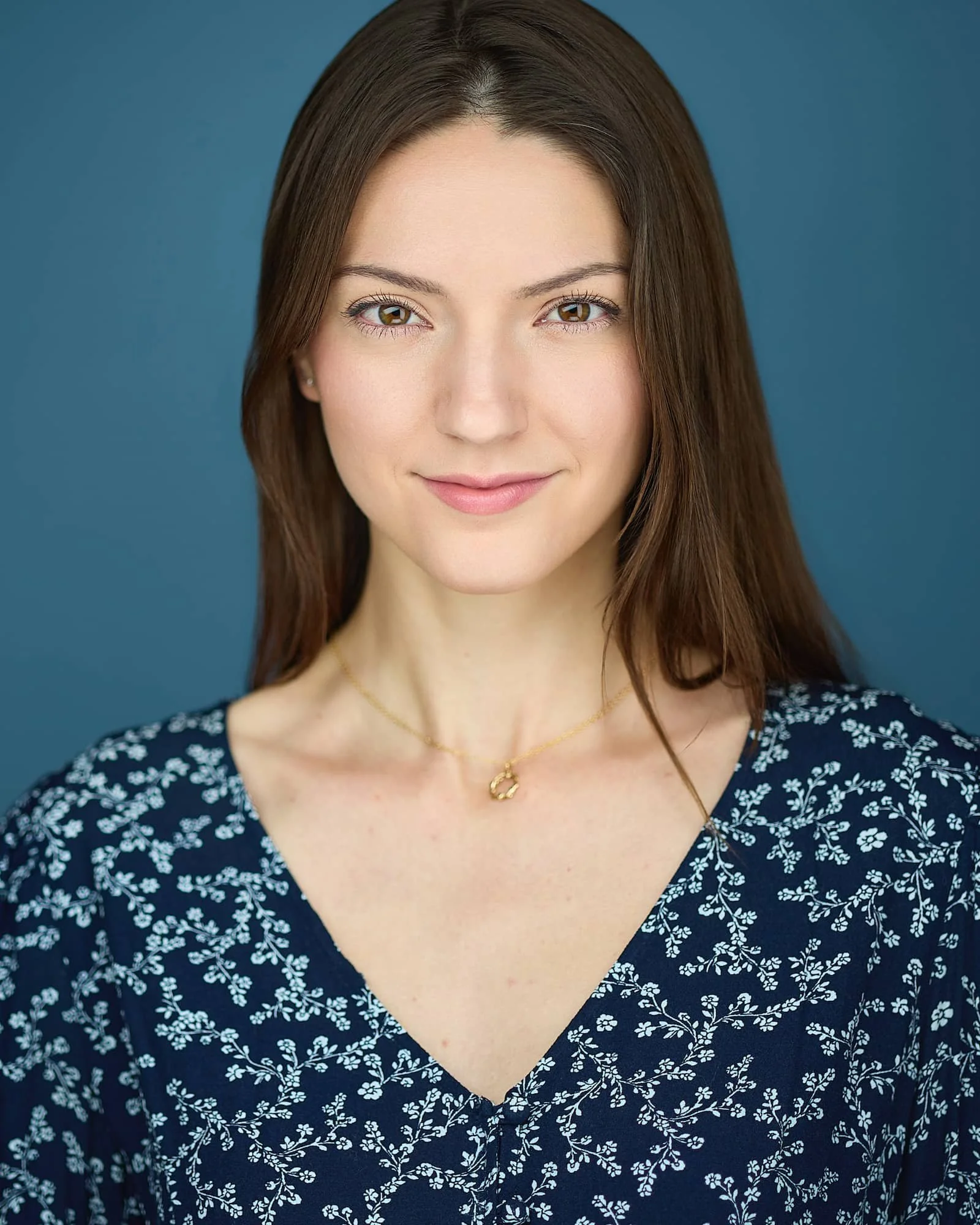 Commercial headshot of an actress wearing a blue floral shirt against a blue backdrop