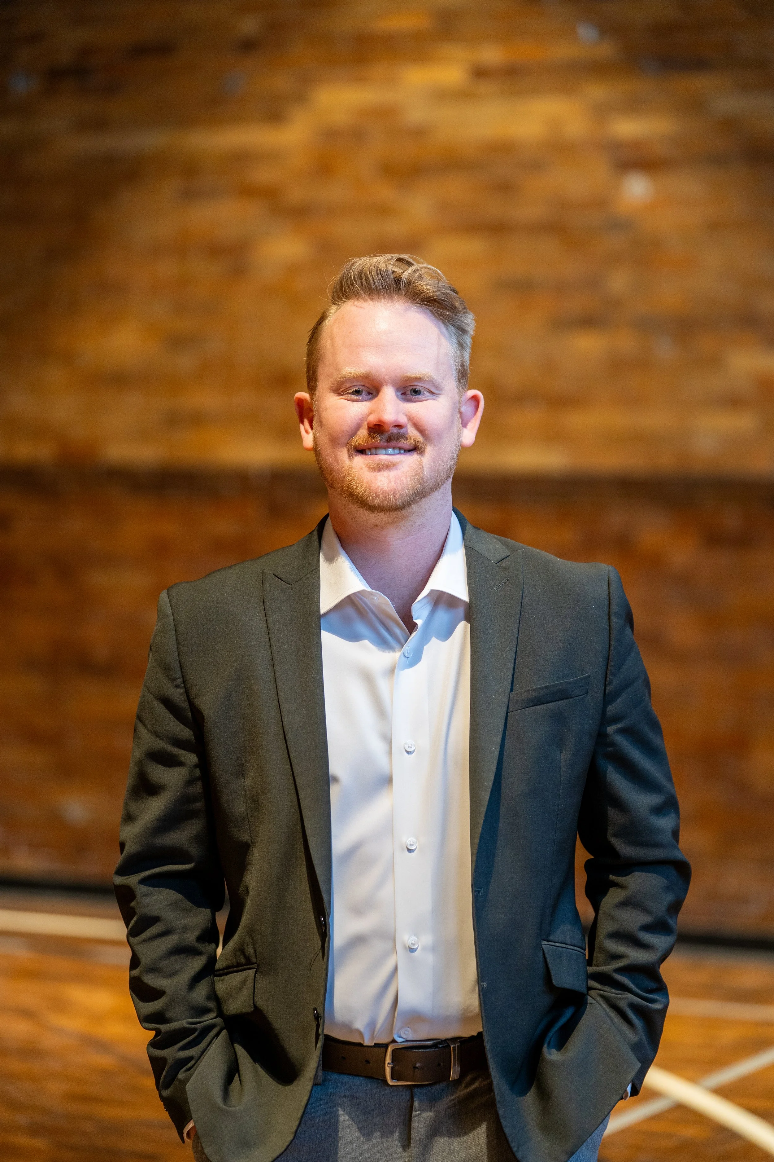 A man in a suit smiling in front of a brick wall