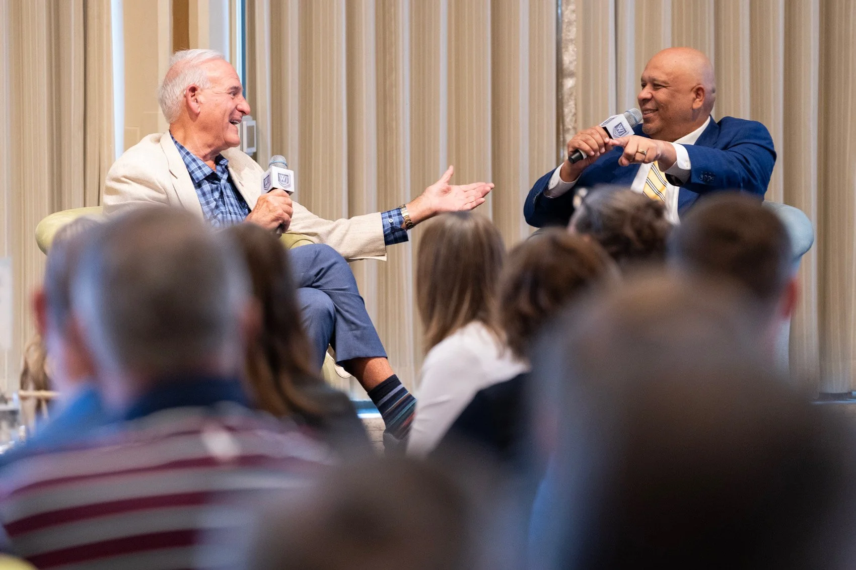 Panel discussion with two men on a stage and an audience seated facing them in a conference room.