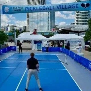 People playing pickleball on an outdoor court in Milwaukee at Summerfest, with city skyscrapers and a blue sky in the background.