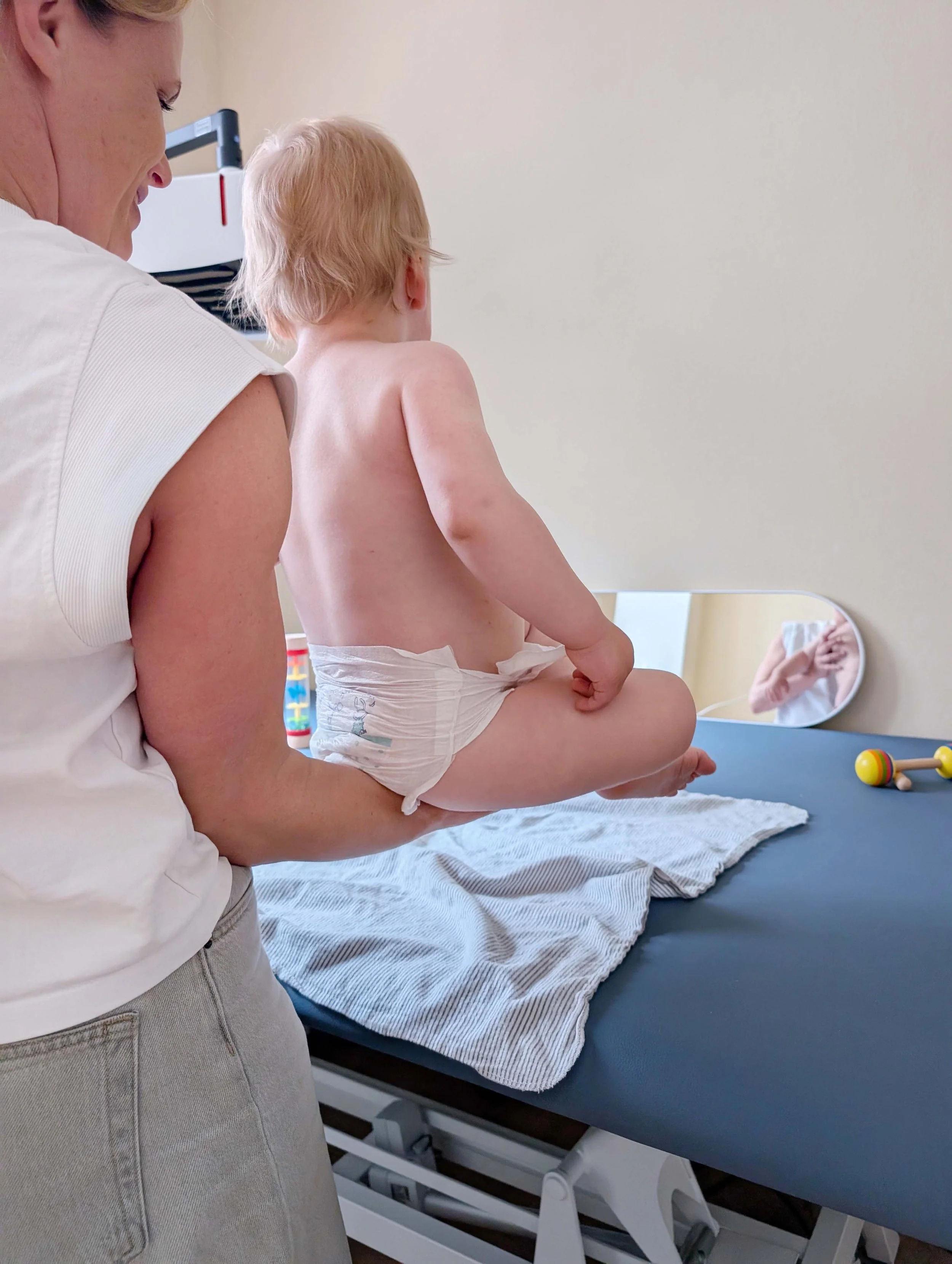 Physiotherapeutin für Kinder steht vor einer Behandlungsliege und hält ein Kind - Foto: Leandra Busch