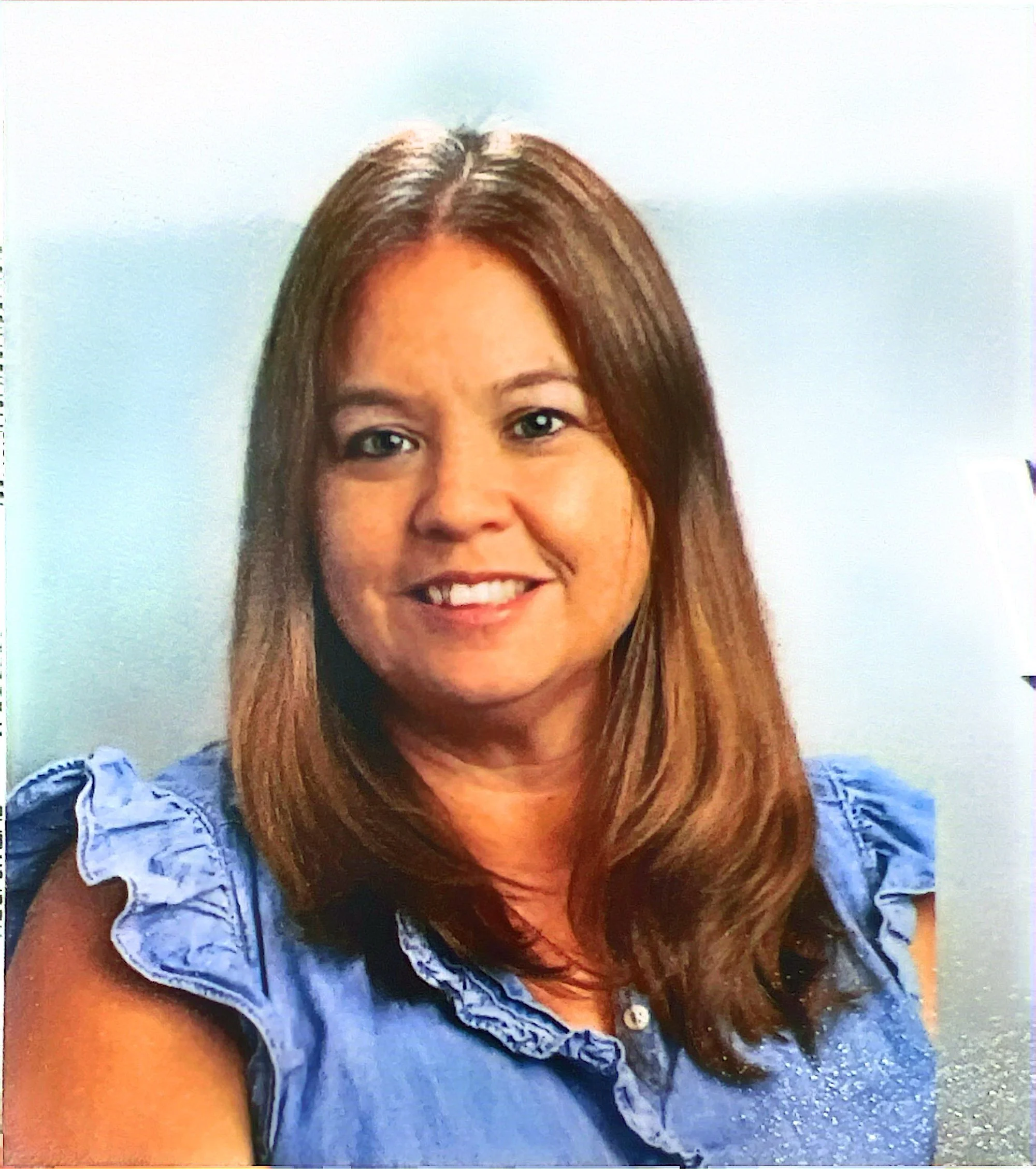 A woman with shoulder-length light brown hair, wearing a blue sleeveless ruffled top, smiling against a neutral background.